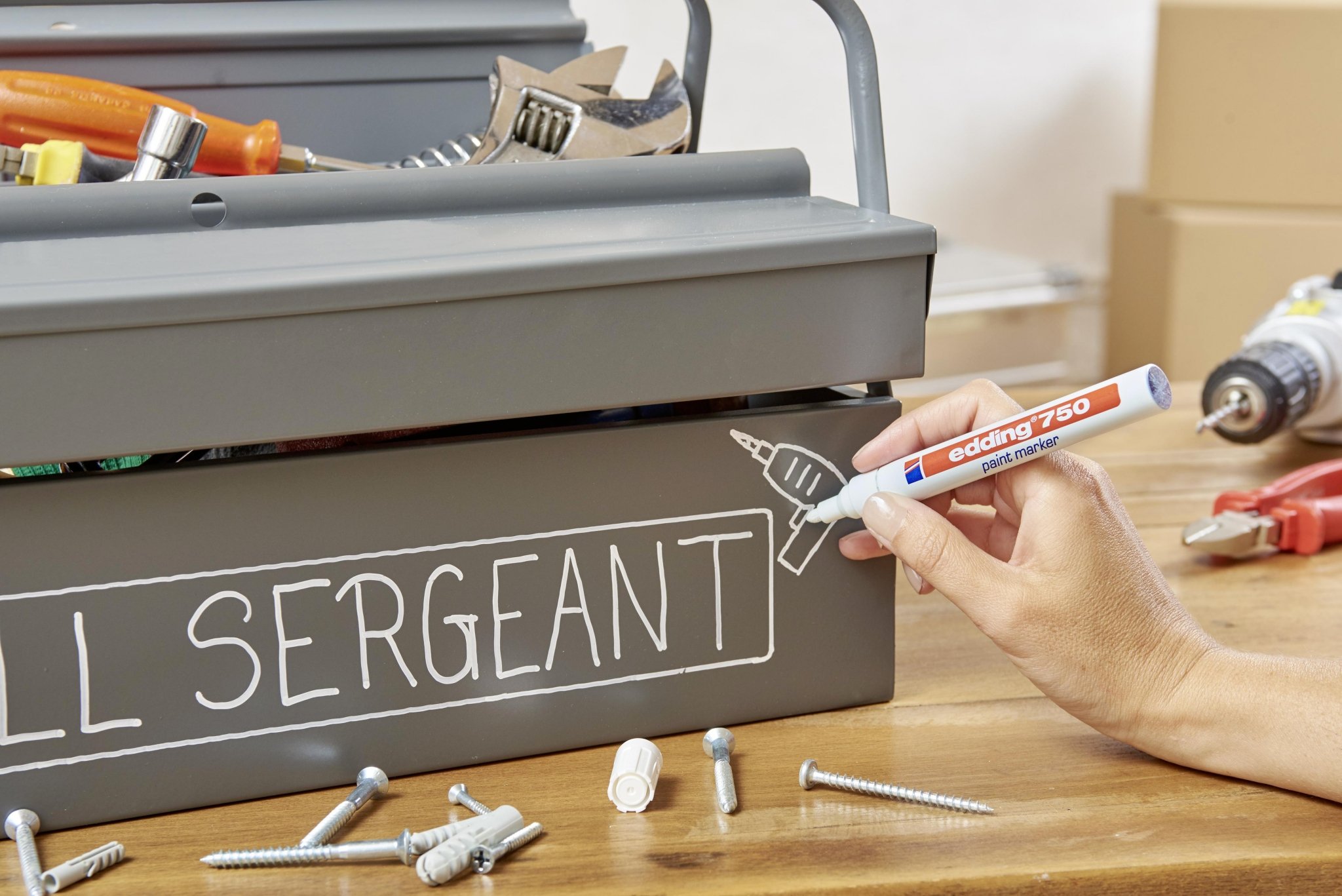 Eine Hand zeichnet mit einem Stift ein Werkzeug auf einen Werkzeugkasten.