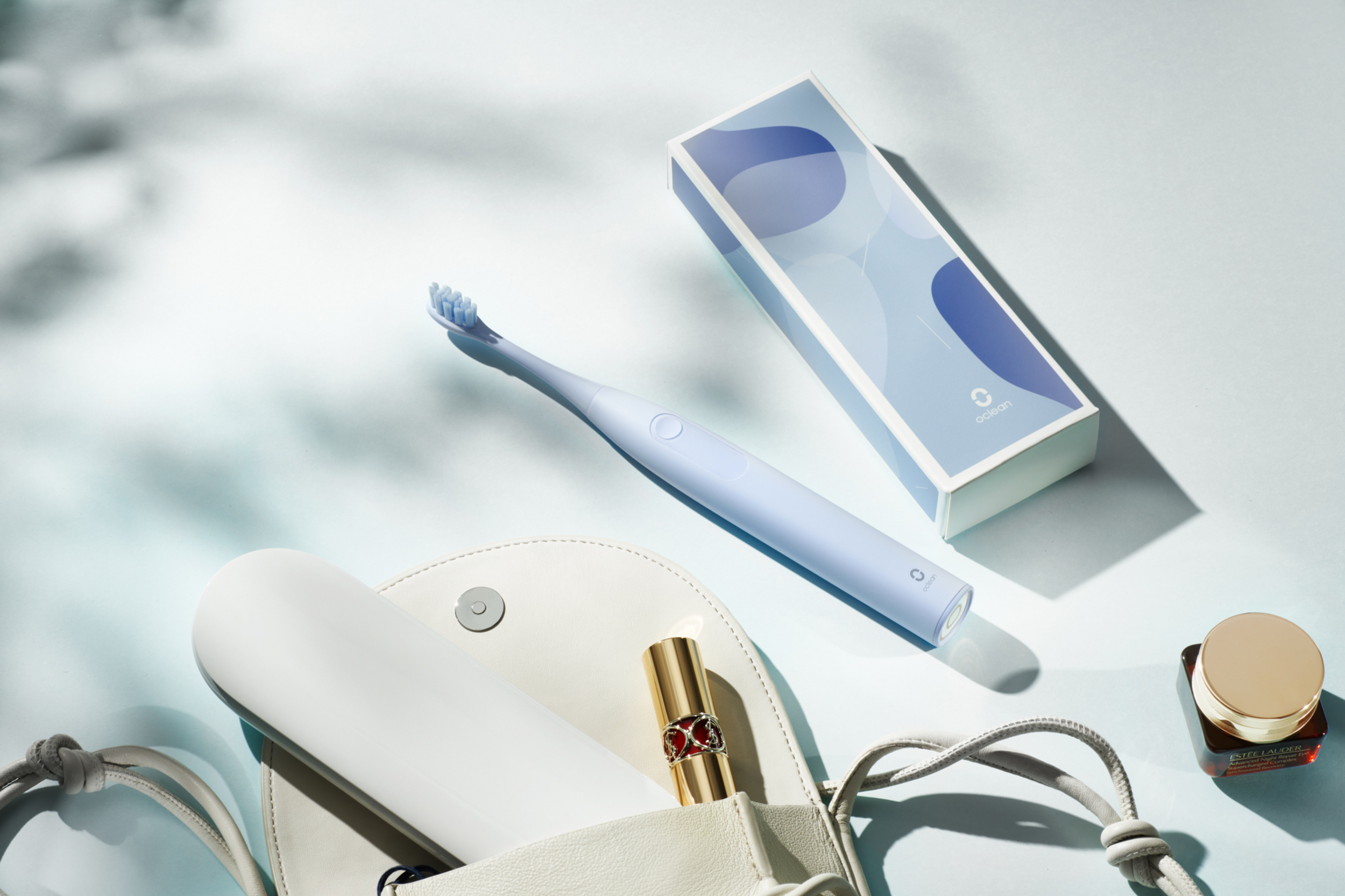 Ein hellblaues Elektrorasierer mit Verpackung, Lippenstift und Kosmetikdose auf blauem Hintergrund.