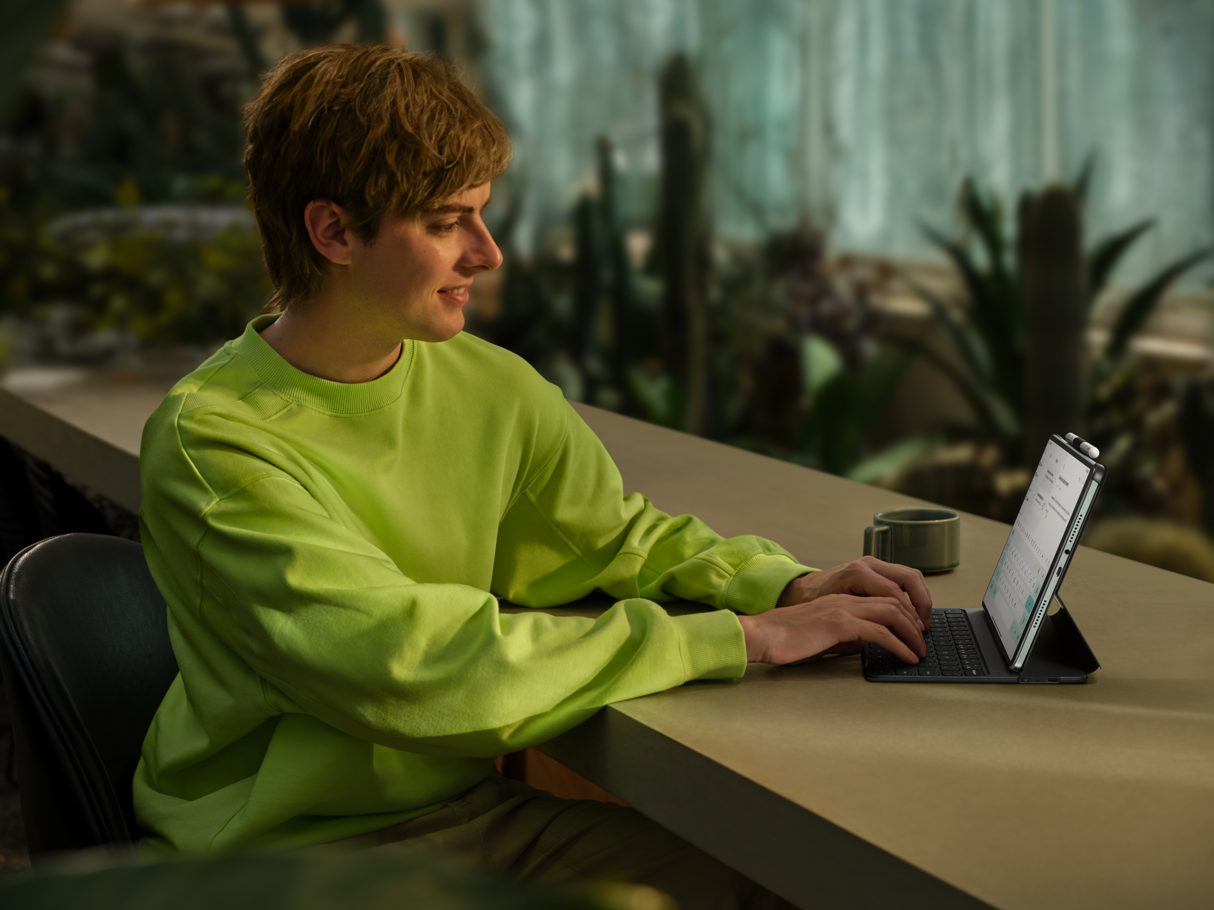 Mężczyzna w limonkowo-zielonej bluzie pisze na tablecie z klawiaturą w szklarni.