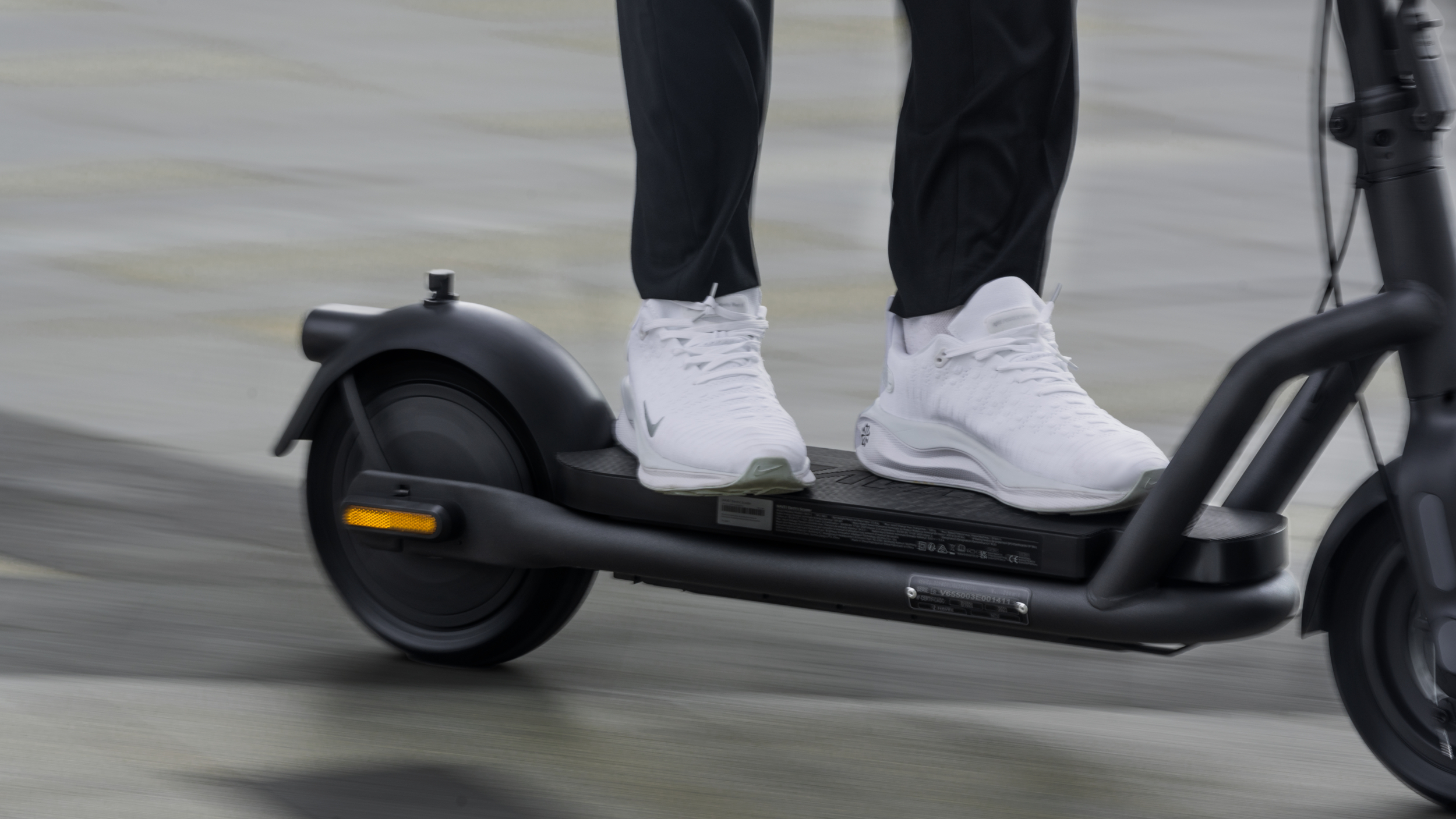 Person fährt auf einem schwarzen Elektroroller mit weißen Turnschuhen.