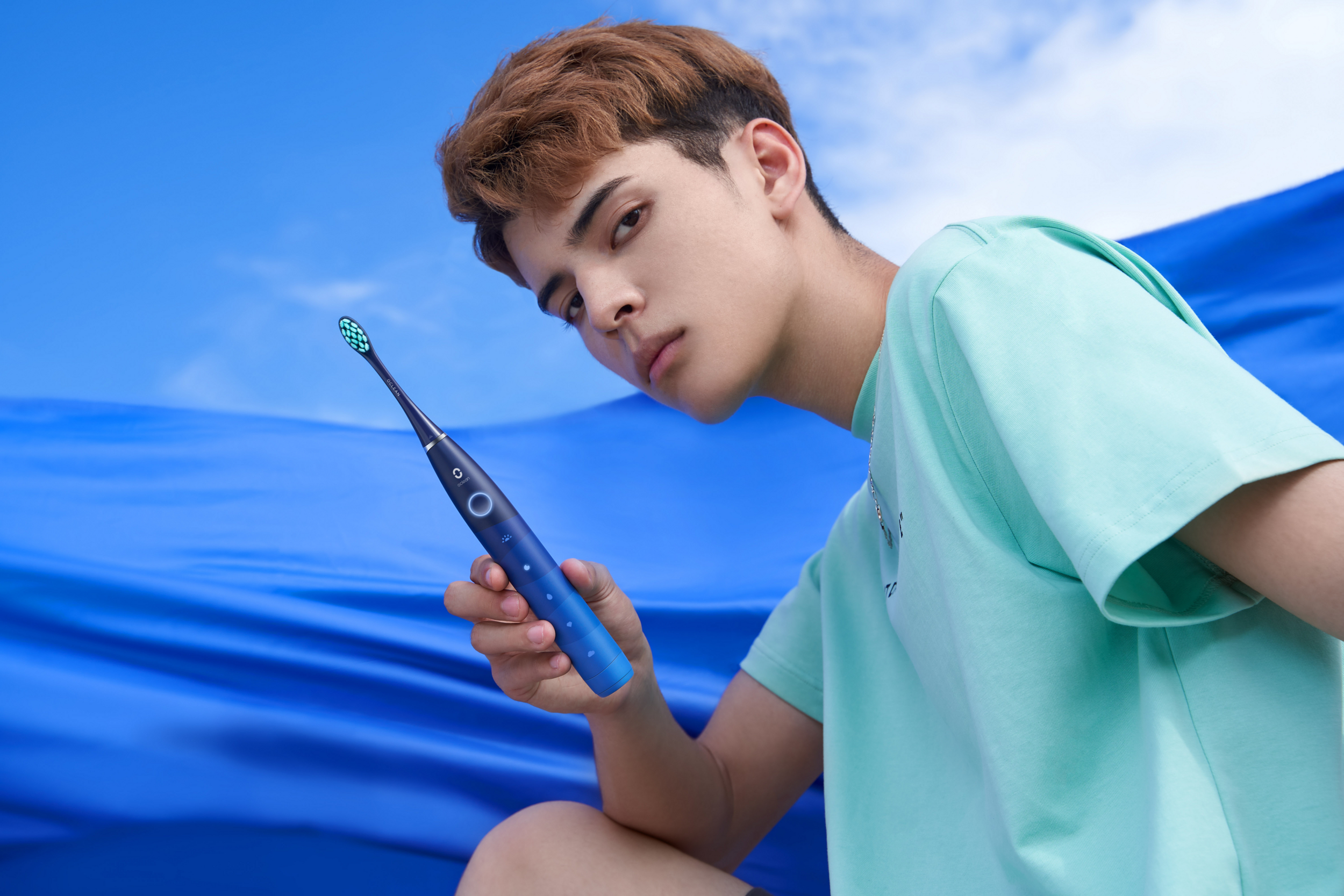 Mężczyzna trzyma niebieską szczoteczkę elektryczną na niebieskim tle.