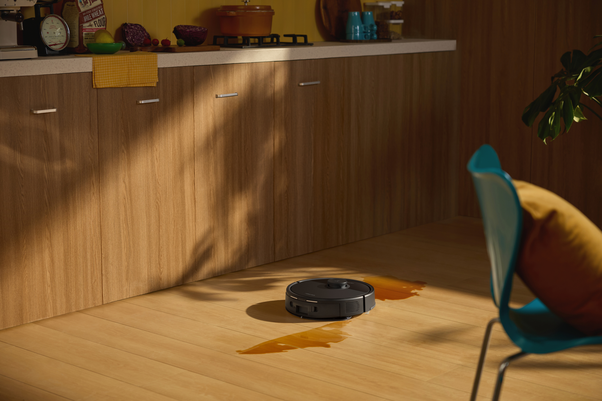 A black robot vacuum cleans spilled liquid on a wooden floor.