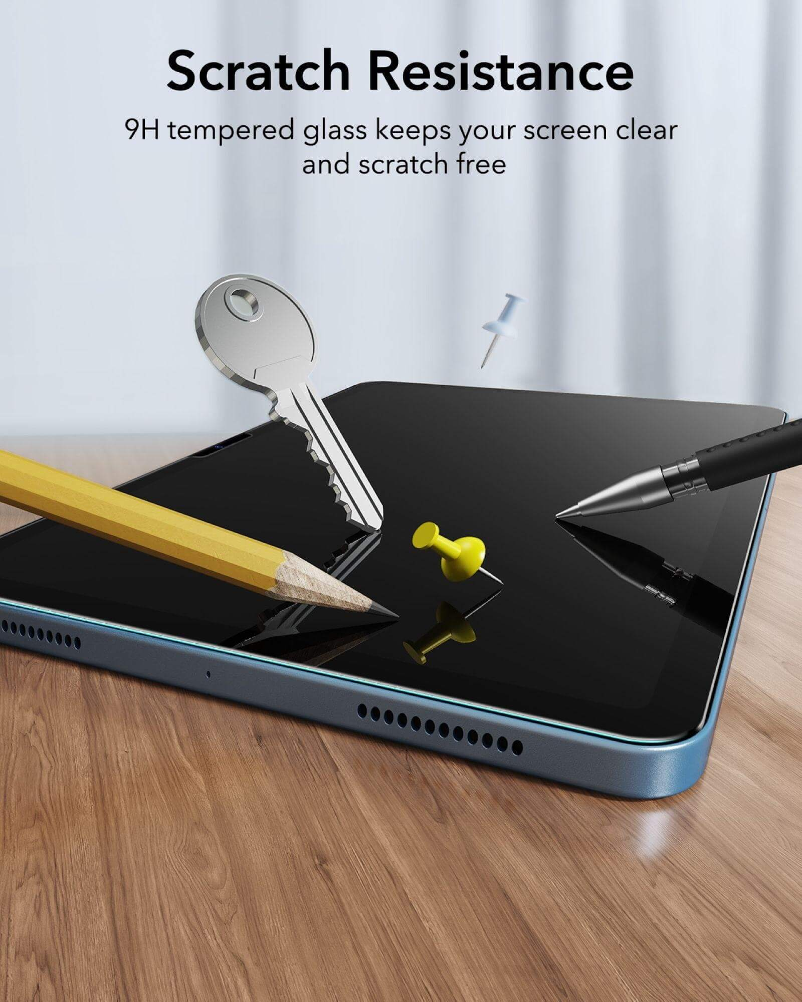 Un tablet con pellicola protettiva, con chiave, matita e due puntine sulla superficie.