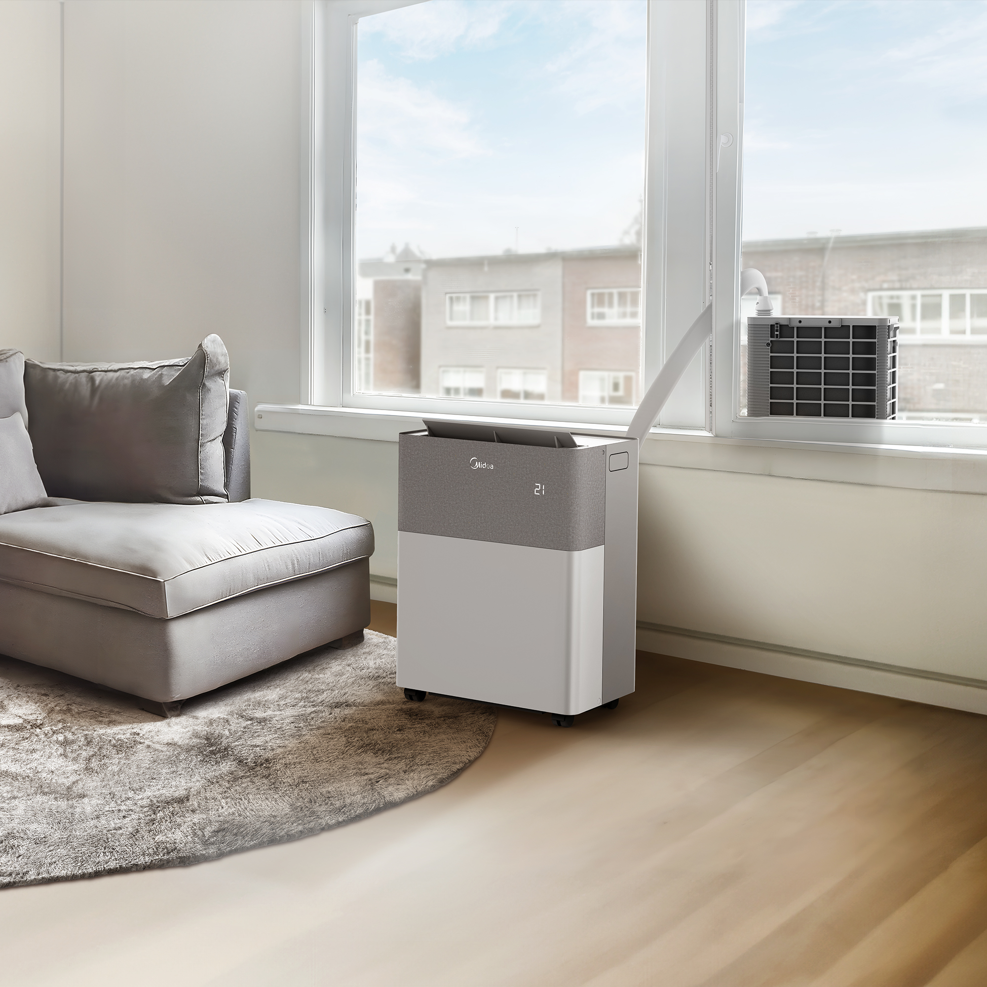 A portable air conditioner sits by a window, with a couch in front.