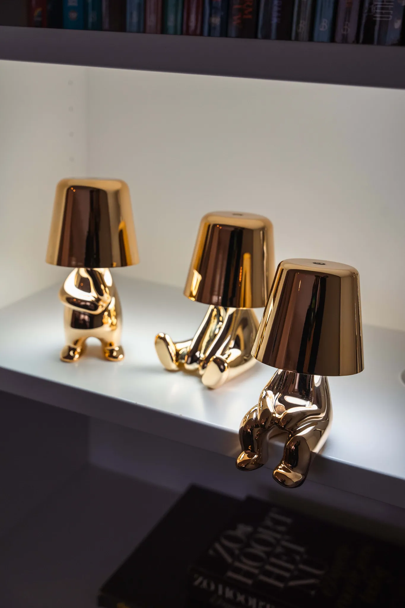 Drei goldene Lampen in Form von sitzenden Figuren stehen auf einem Regal.