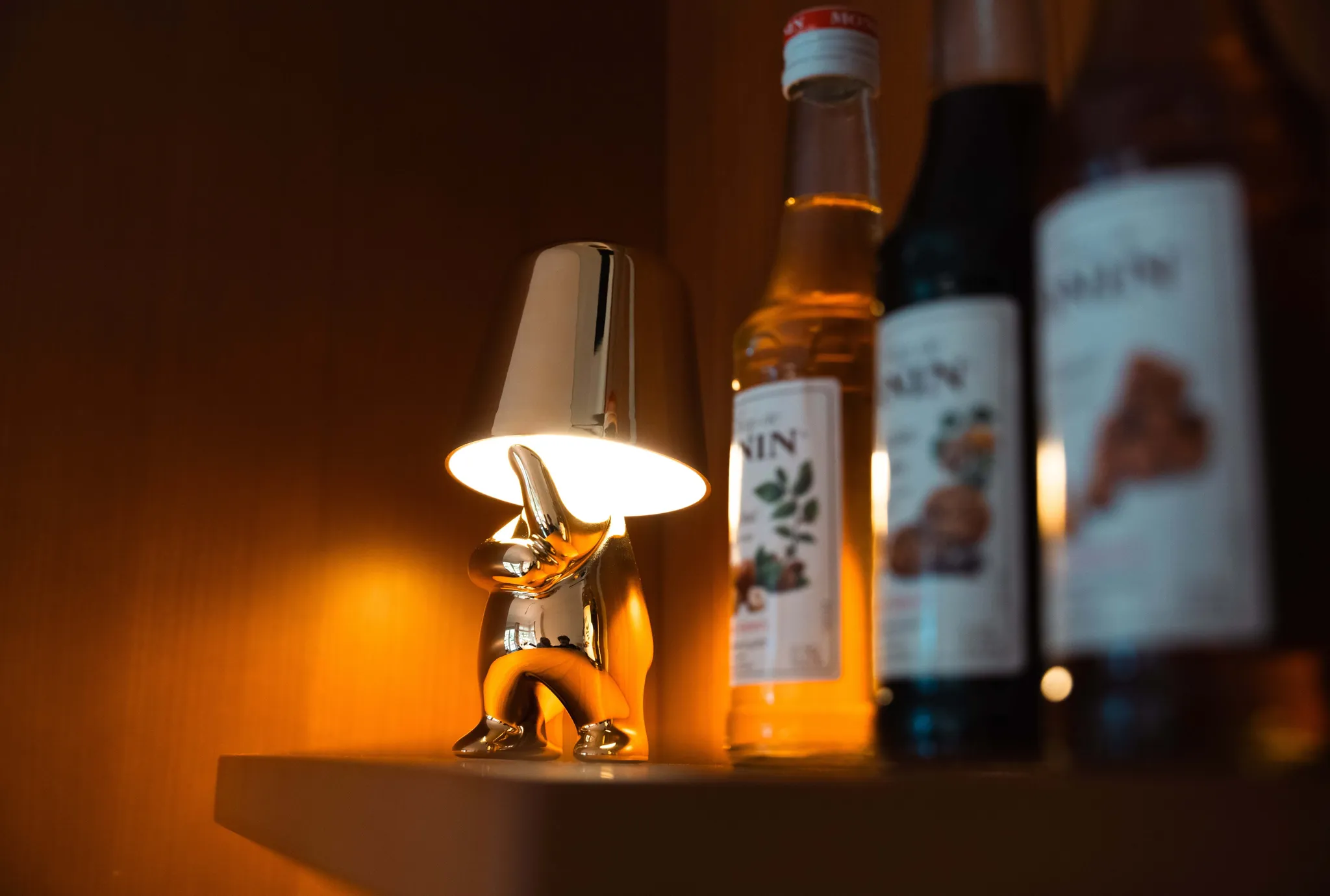 Eine goldene Lampe in Elefantenform leuchtet neben drei Flaschen auf einem Regal.