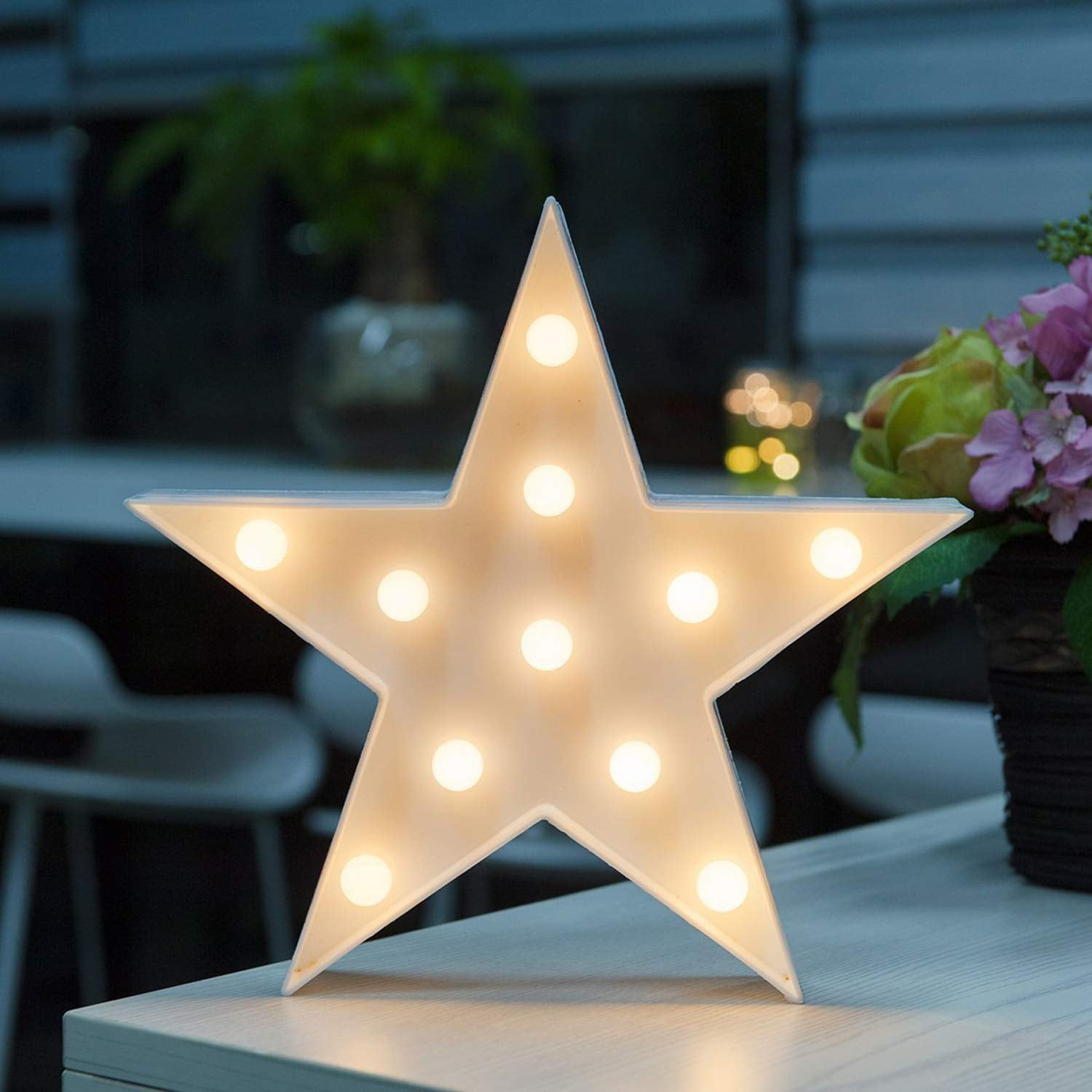 Eine weiße Sternlampe mit Glühbirnen leuchtet auf einem Tisch, Blumen im Hintergrund.
