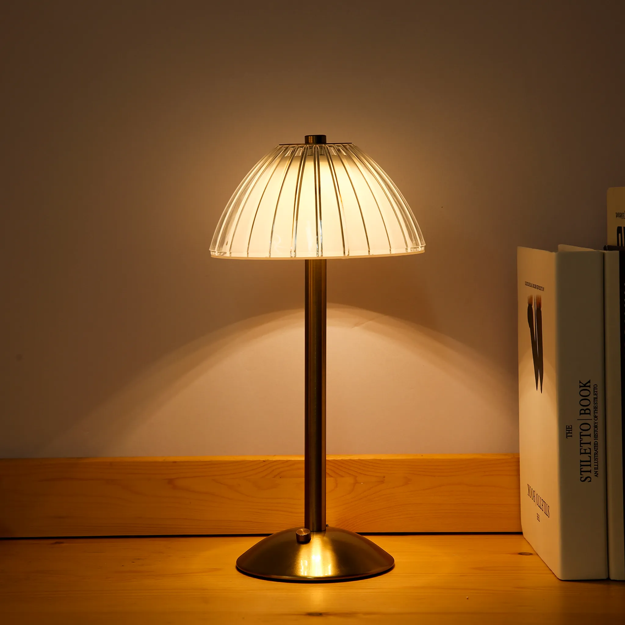 Eine Tischlampe mit geripptem Glas-Schirm und Messingfuß steht neben Büchern.