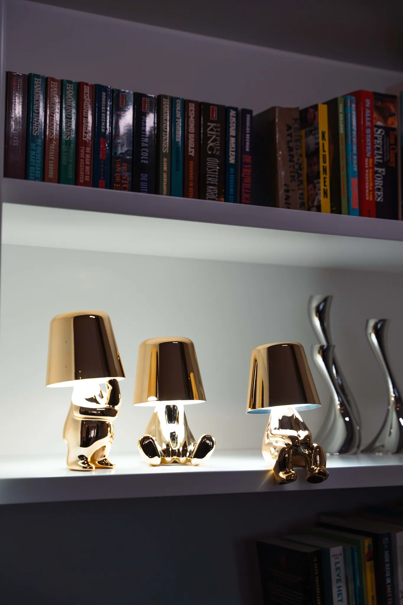 Goldene Lampen in Bärenform stehen auf einem Regal neben Büchern und Vasen.