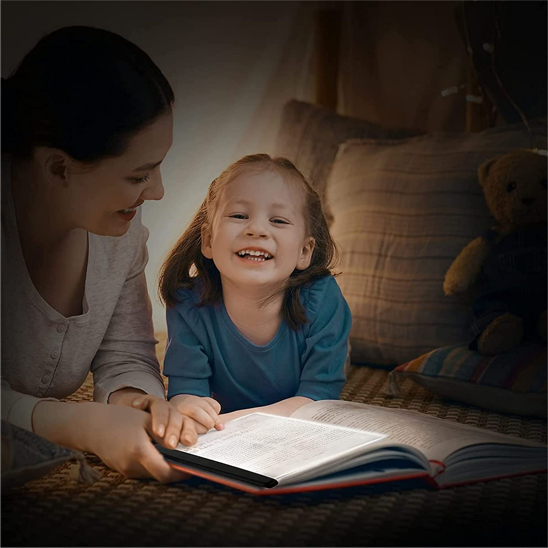 Mutter liest kleinem Mädchen ein Buch vor, Teddy im Hintergrund.