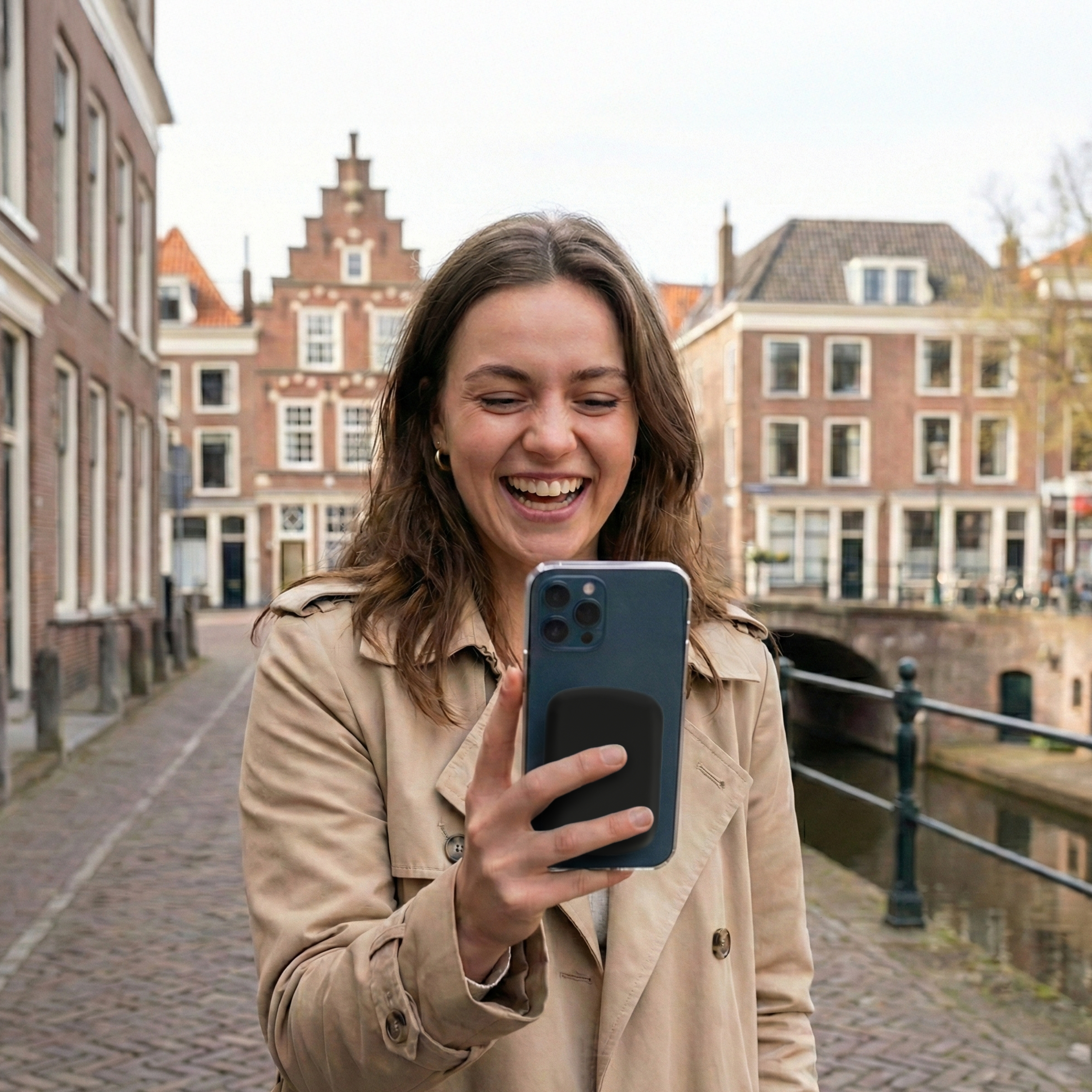 Une femme riant tient un smartphone dans une rue avec des canaux et des bâtiments.