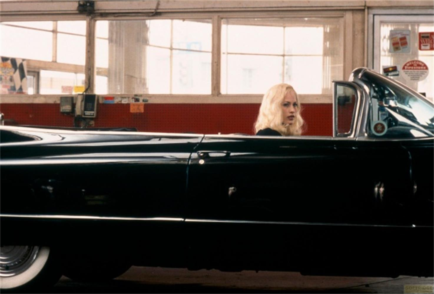 Una donna bionda seduta in un'auto d'epoca nera.