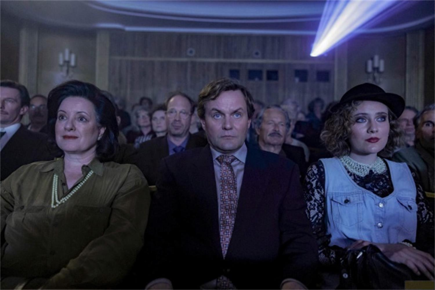 Persone sedute in un cinema buio guardano avanti. Un raggio di luce brilla dall'alto.
