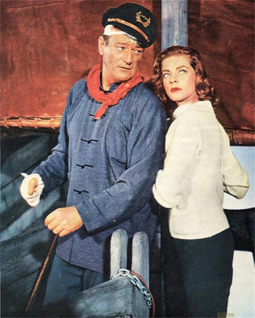 Uomo con berretto da capitano e donna in maglione bianco su una nave.