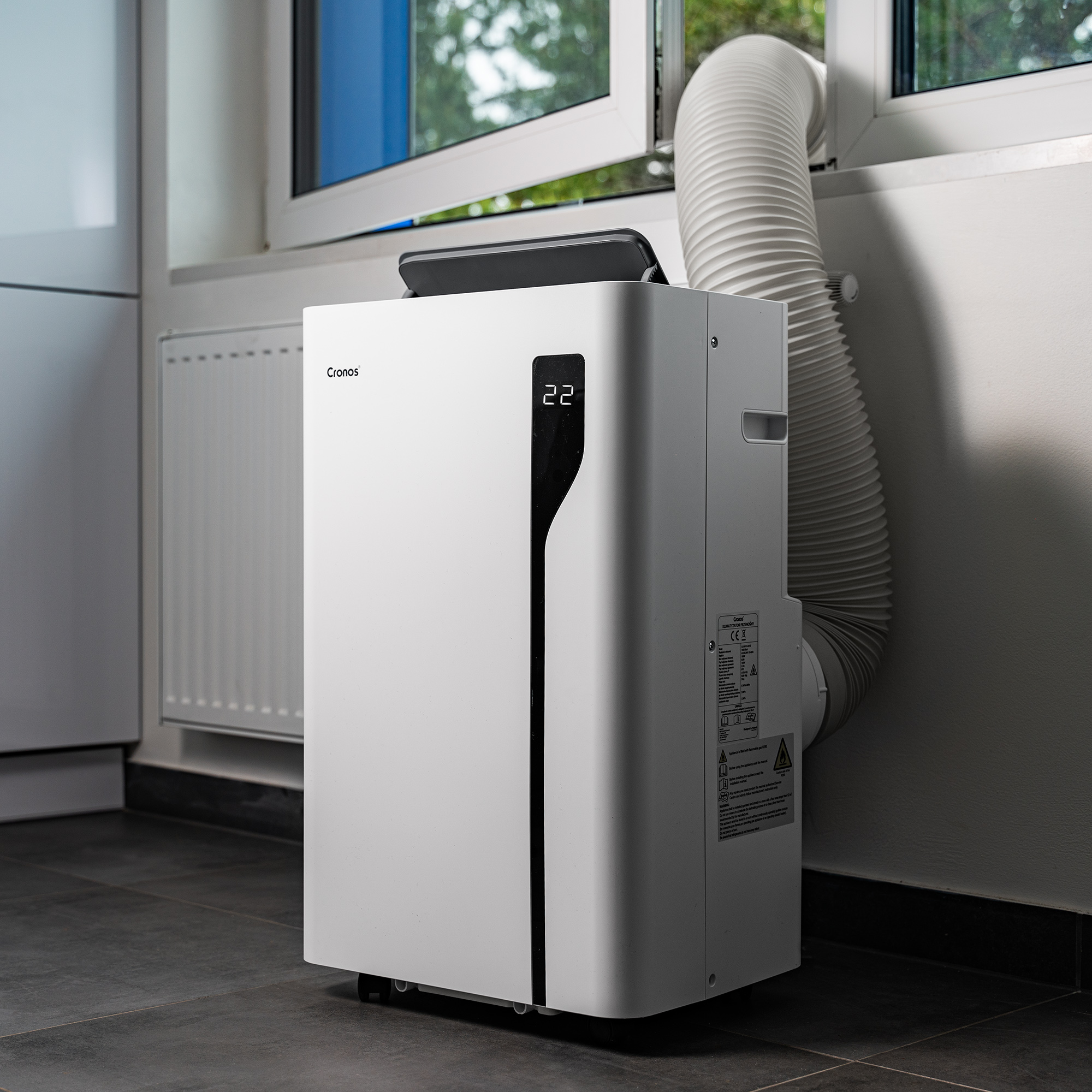 Biała przenośna jednostka klimatyzacyjna z elastycznym wężem wychodzącym z okna.