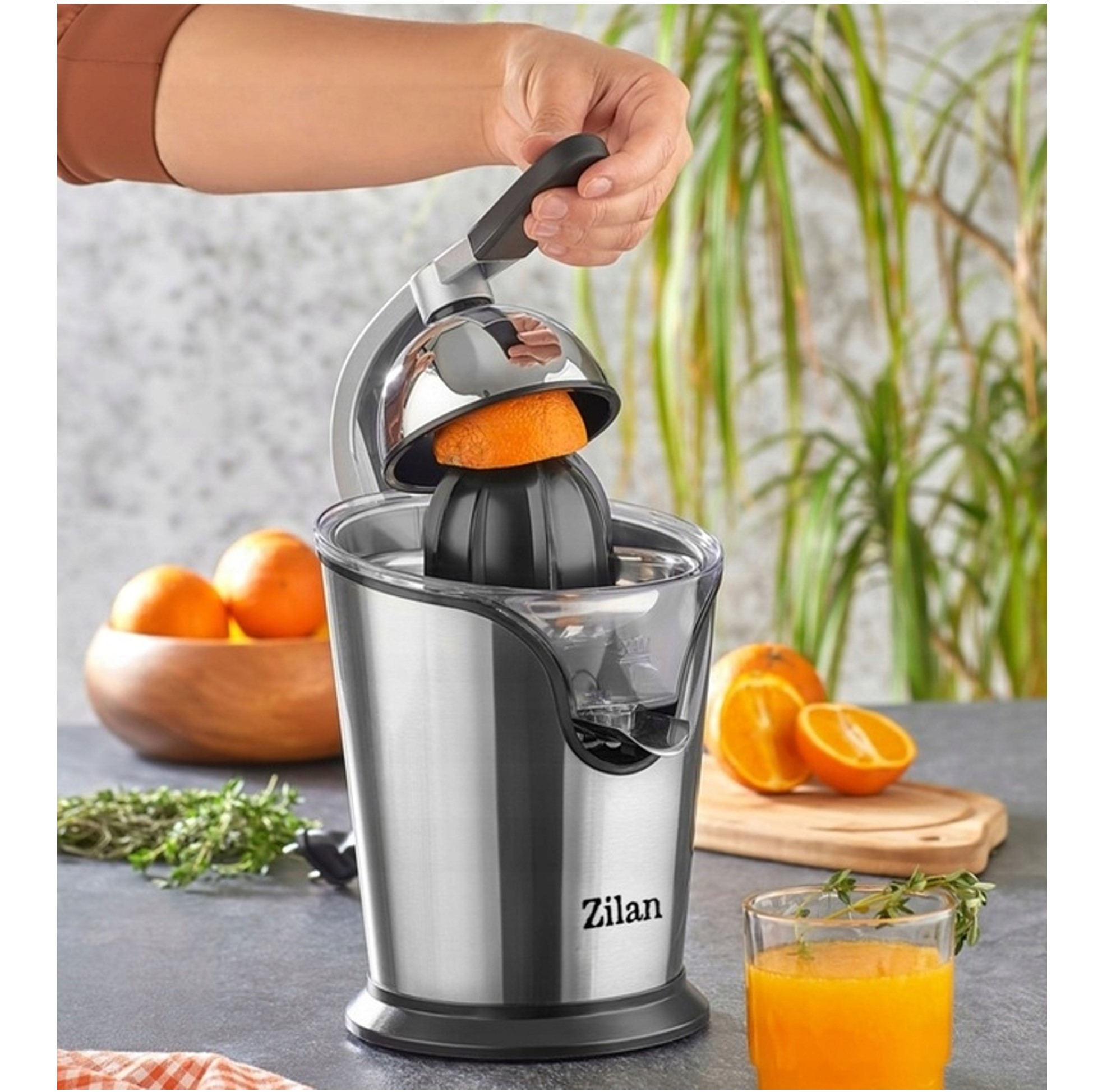 Ręka naciska wyciskarkę z pomarańczą. Sok pomarańczowy w szklance.