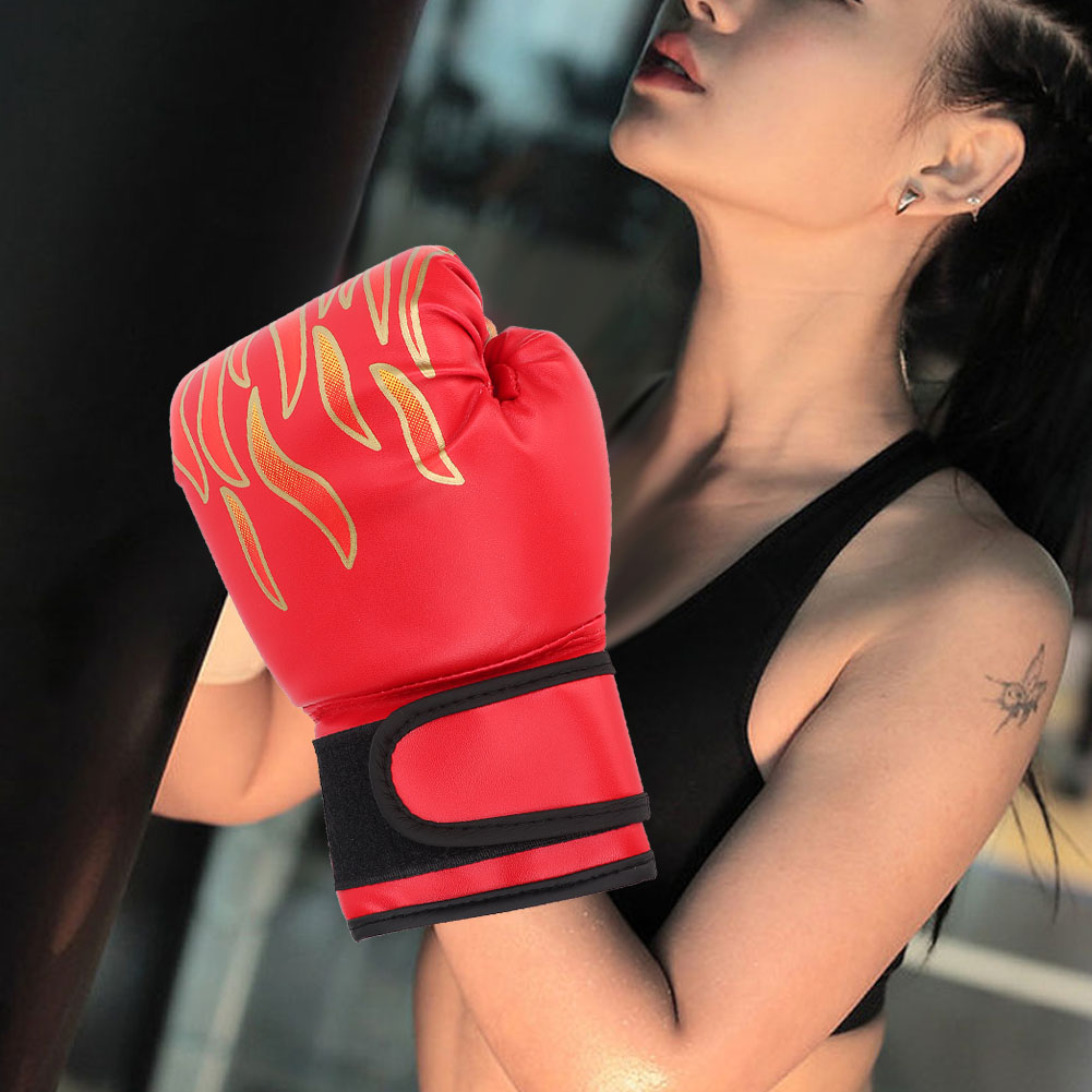 Eine Frau in einem schwarzen Sport-BH trägt einen roten Boxhandschuh mit goldenen Flammenmustern und steht neben einem schwarzen Boxsack.