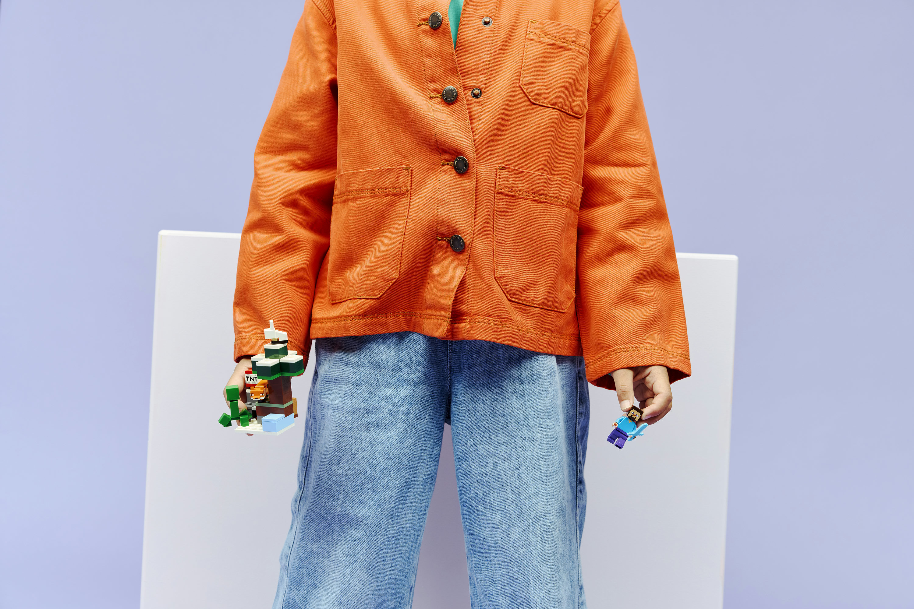 Osoba w pomarańczowej kurtce trzyma figurki Minecraft, jedną z TNT, drugą z mieczem.