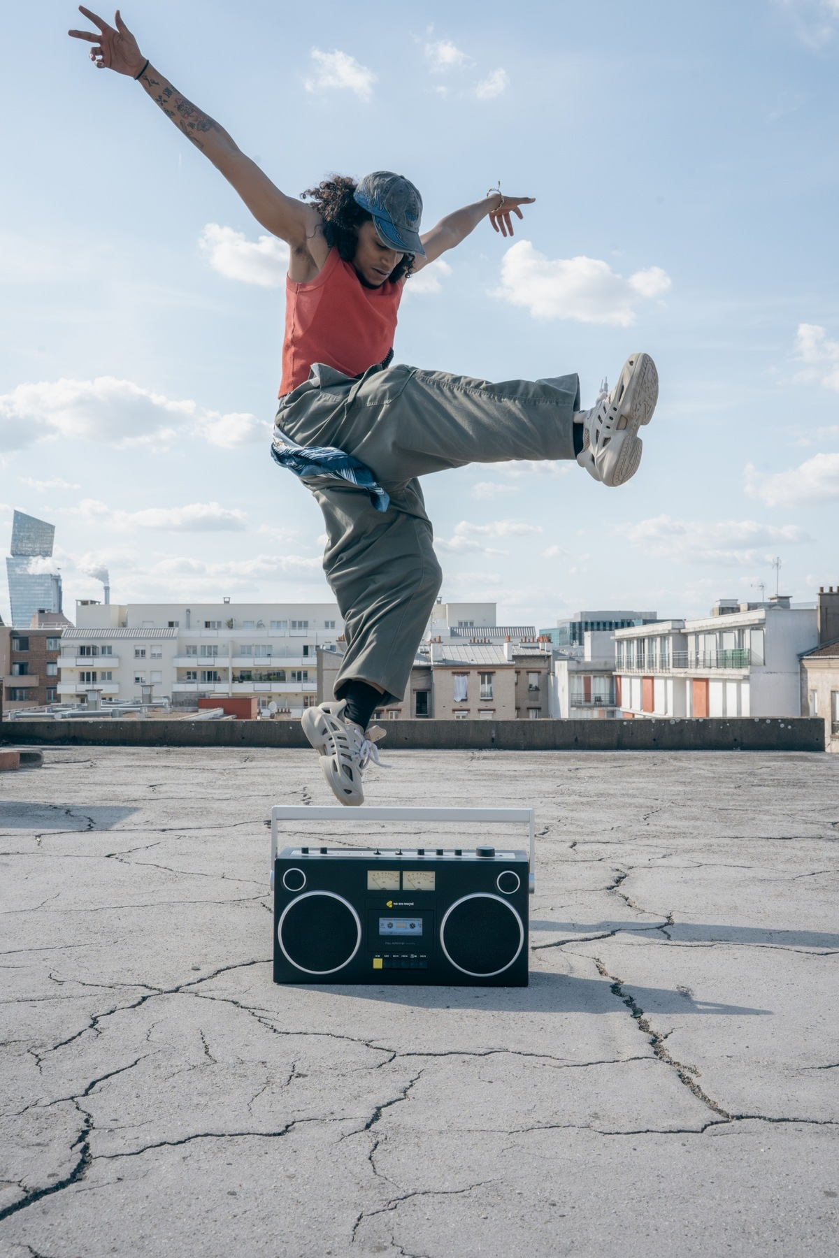 Tänzer springt über Boombox auf Dach vor Stadtsilhouette.