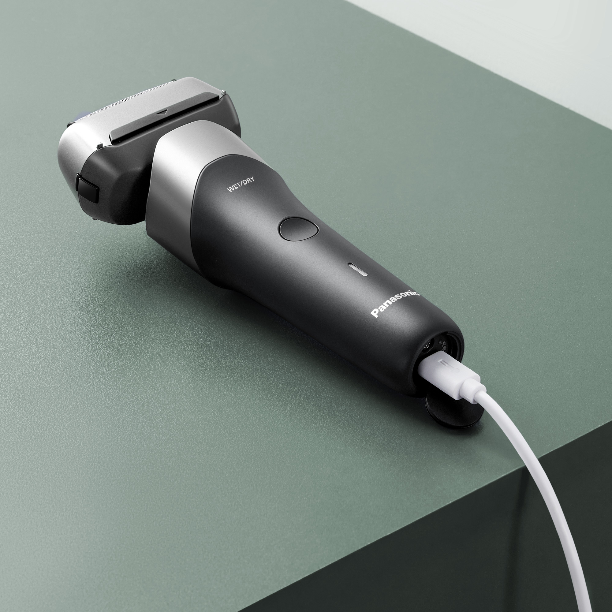 Ein schwarzer Panasonic Rasierer mit silbernen Akzenten und einem weißen Ladekabel.