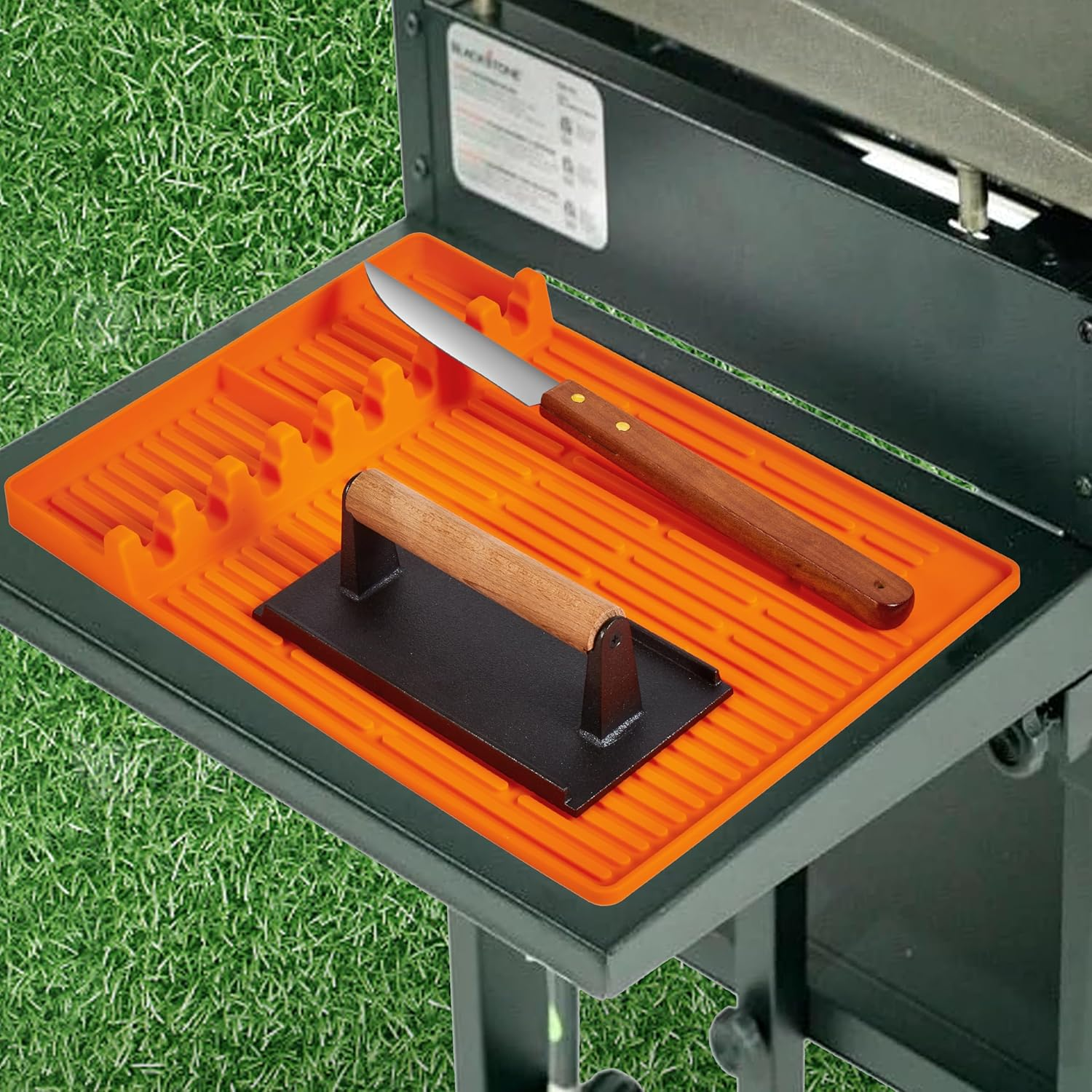Orange Grillzubehörtablett mit einem Burgerpresse und einem Messer auf einem Grill.