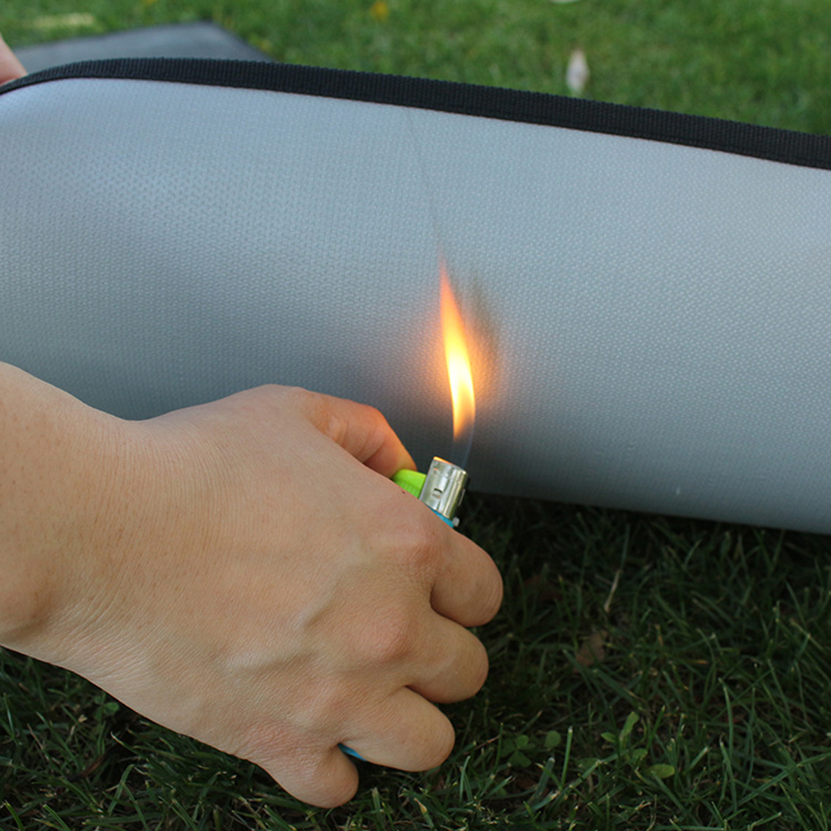Eine Hand hält ein grünes Feuerzeug, das eine Flamme entzündet, vor einem grauen Objekt.