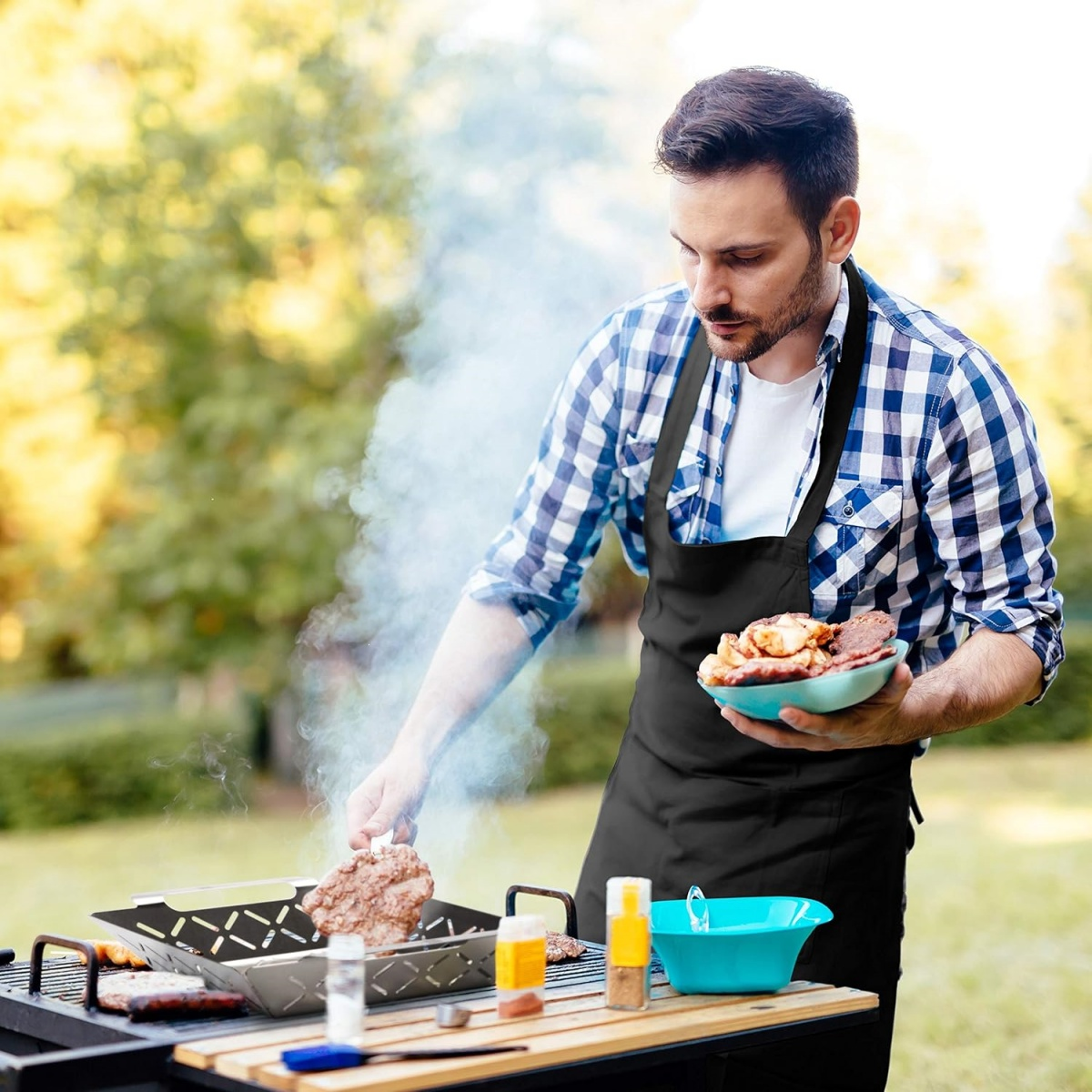 Mann grillt Burger und Fleisch im Garten. Er hält eine Schale mit Fleisch.