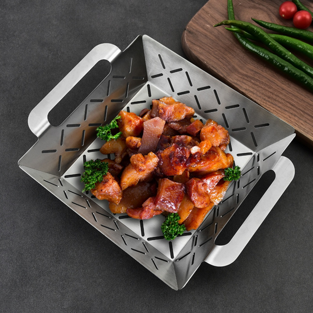 Gegrilltes Fleisch mit Petersilie in einem Metallkorb, daneben grüne Chilis auf einem Holzbrett.