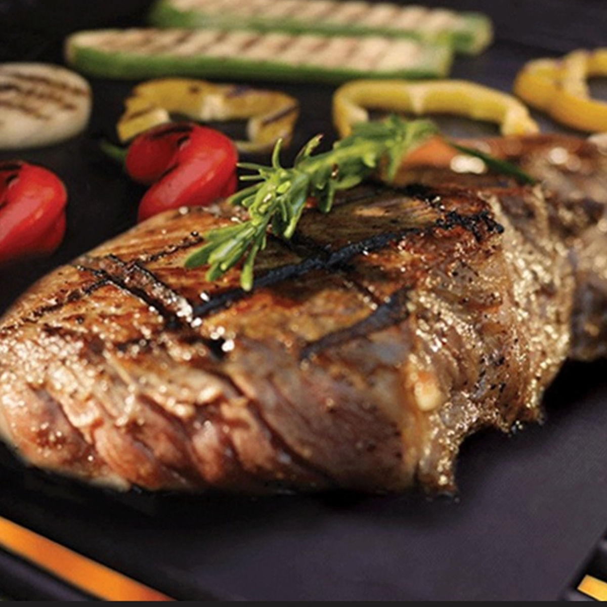 Ein gegrilltes Steak mit Rosmarin und verschwommenem Gemüse auf einem Grill.
