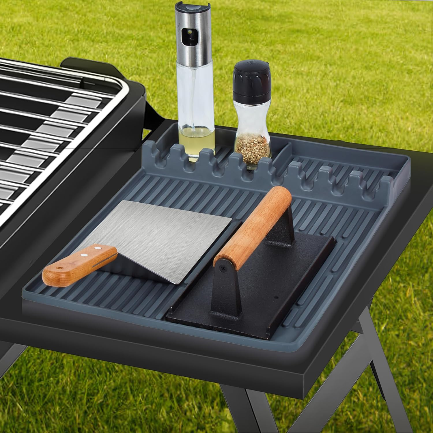 Grillzubehör auf einem Tisch: Ölsprüher, Gewürzstreuer, Wender und Burgerpresse.