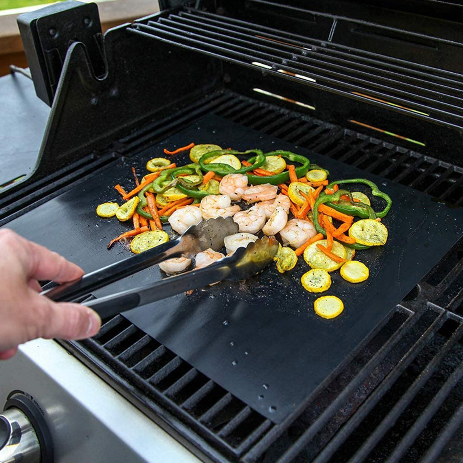 Garnelen und Gemüse werden auf einer Grillmatte mit Zange gegrillt.