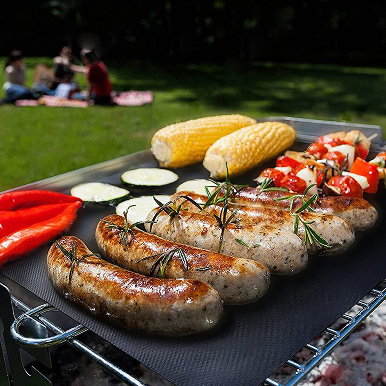 Bratwürste, Maiskolben, Zucchini und Paprika auf einem Grillrost im Freien.