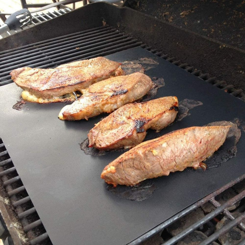 Vier saftige Steaks liegen auf einer schwarzen Grillmatte auf einem Grill.