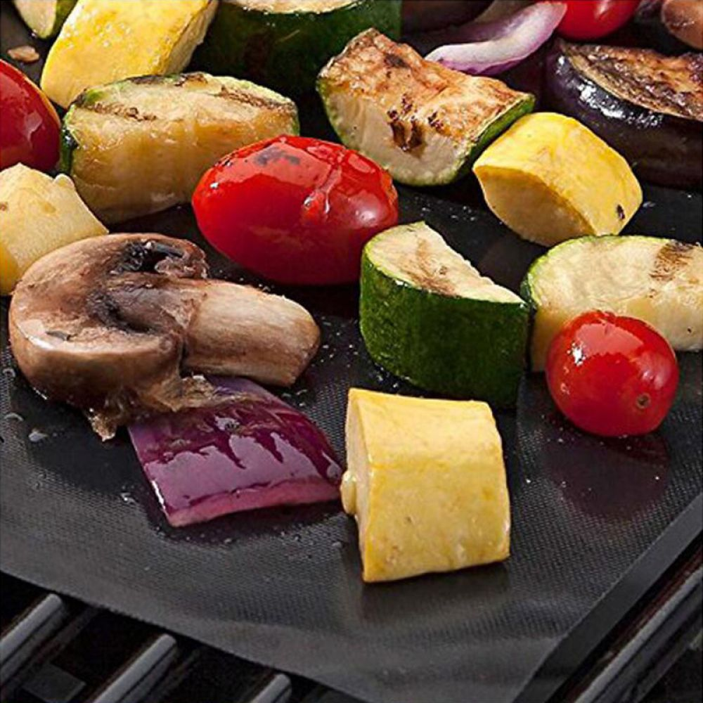 Gegrilltes Gemüse wie Zucchini, Tomaten, Auberginen und Pilze liegen auf einer schwarzen Grillmatte.