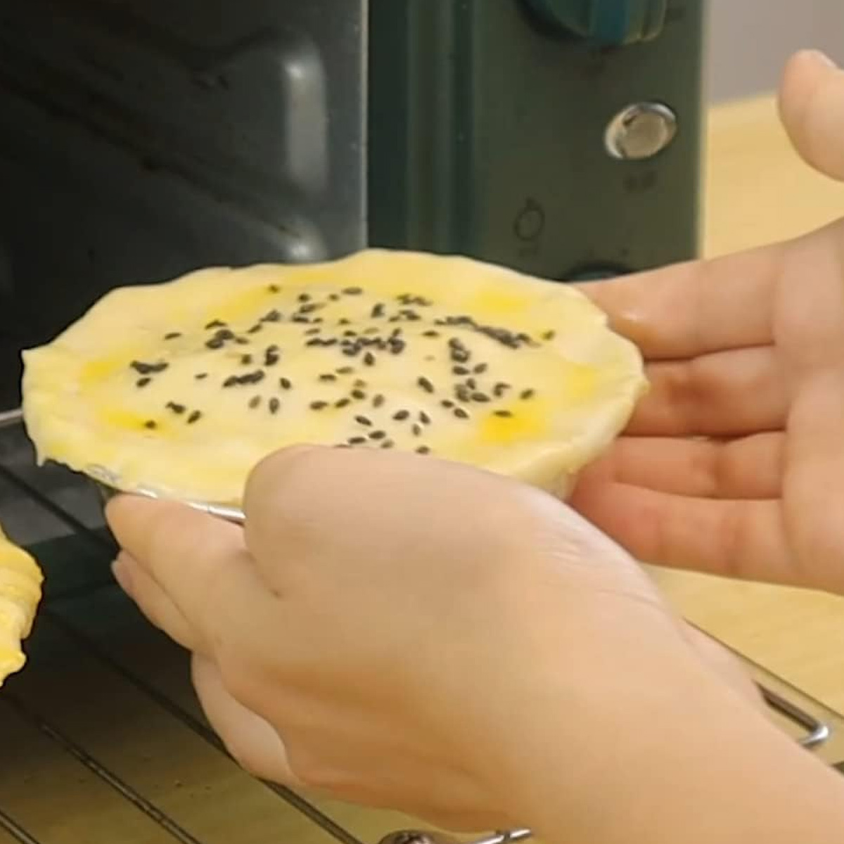 Hände legen einen Kuchen mit Sesam darauf in einen Ofen.