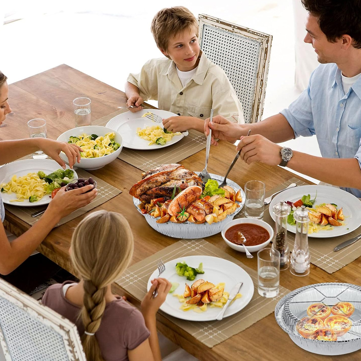 Familie isst am Holztisch, serviert werden Braten, Wurst, Kartoffeln und Pasta.