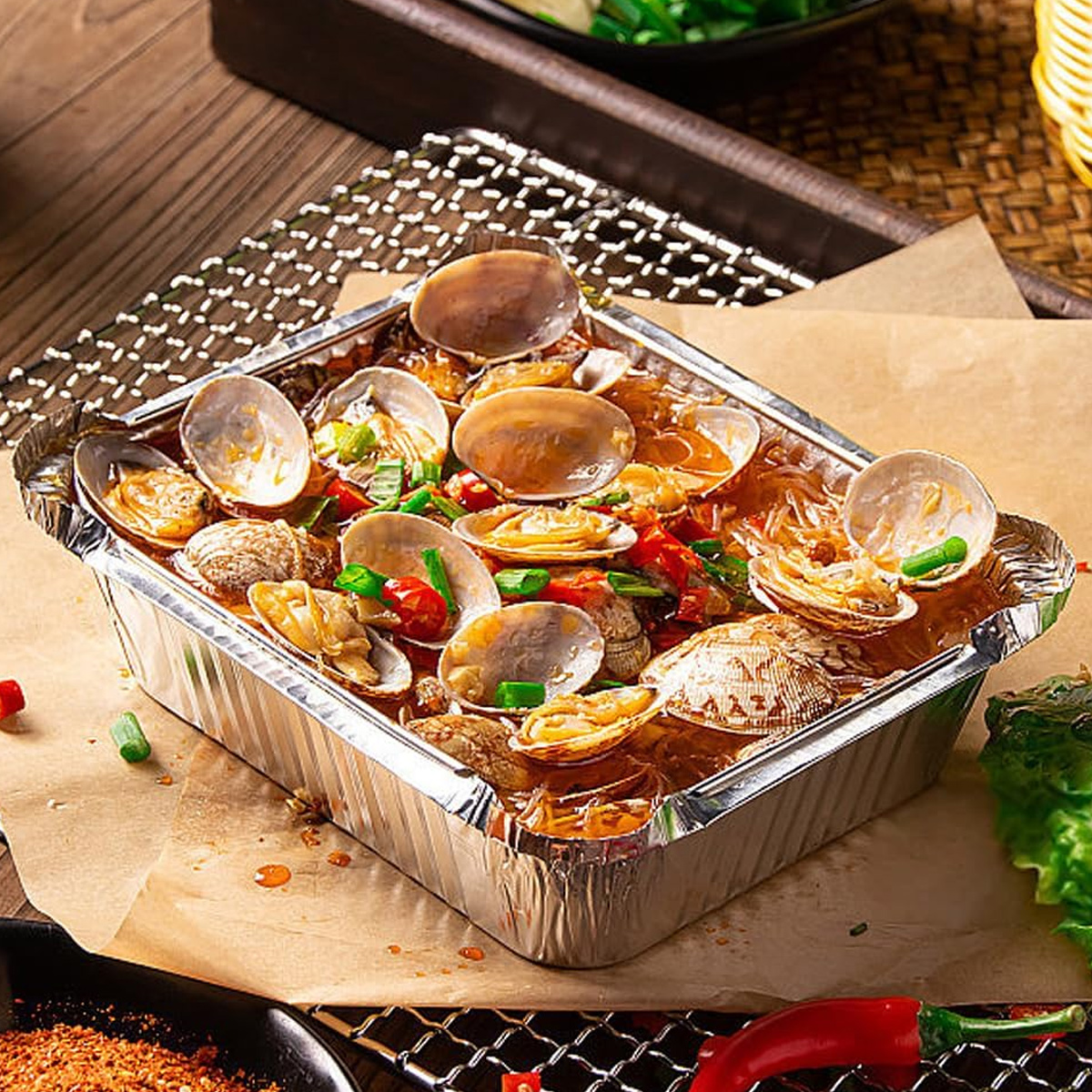 Ein Aluminiumbehälter gefüllt mit Muscheln und Nudeln, garniert mit Frühlingszwiebeln und Chili.