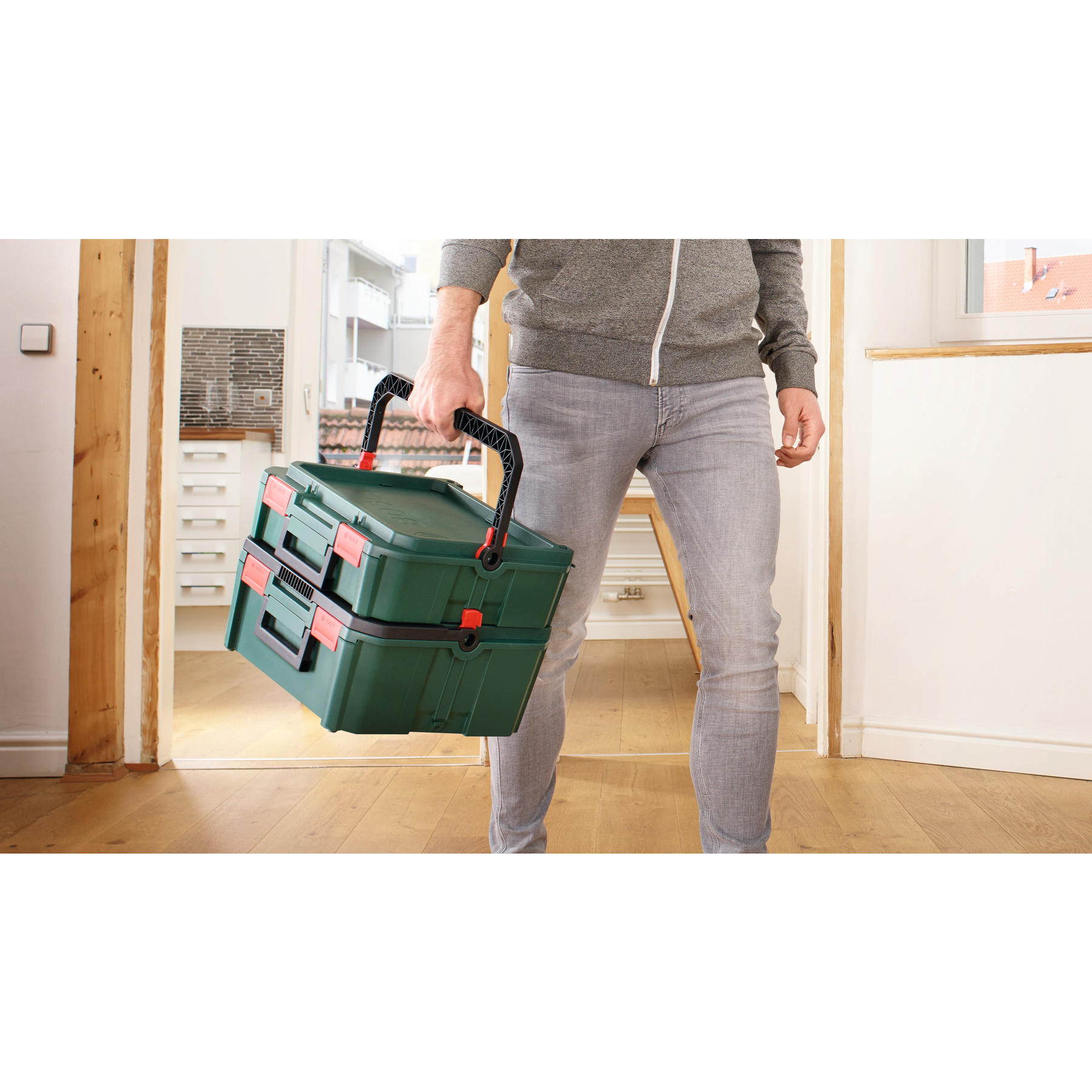 Uomo porta due cassette degli attrezzi verdi con accenti rossi.
