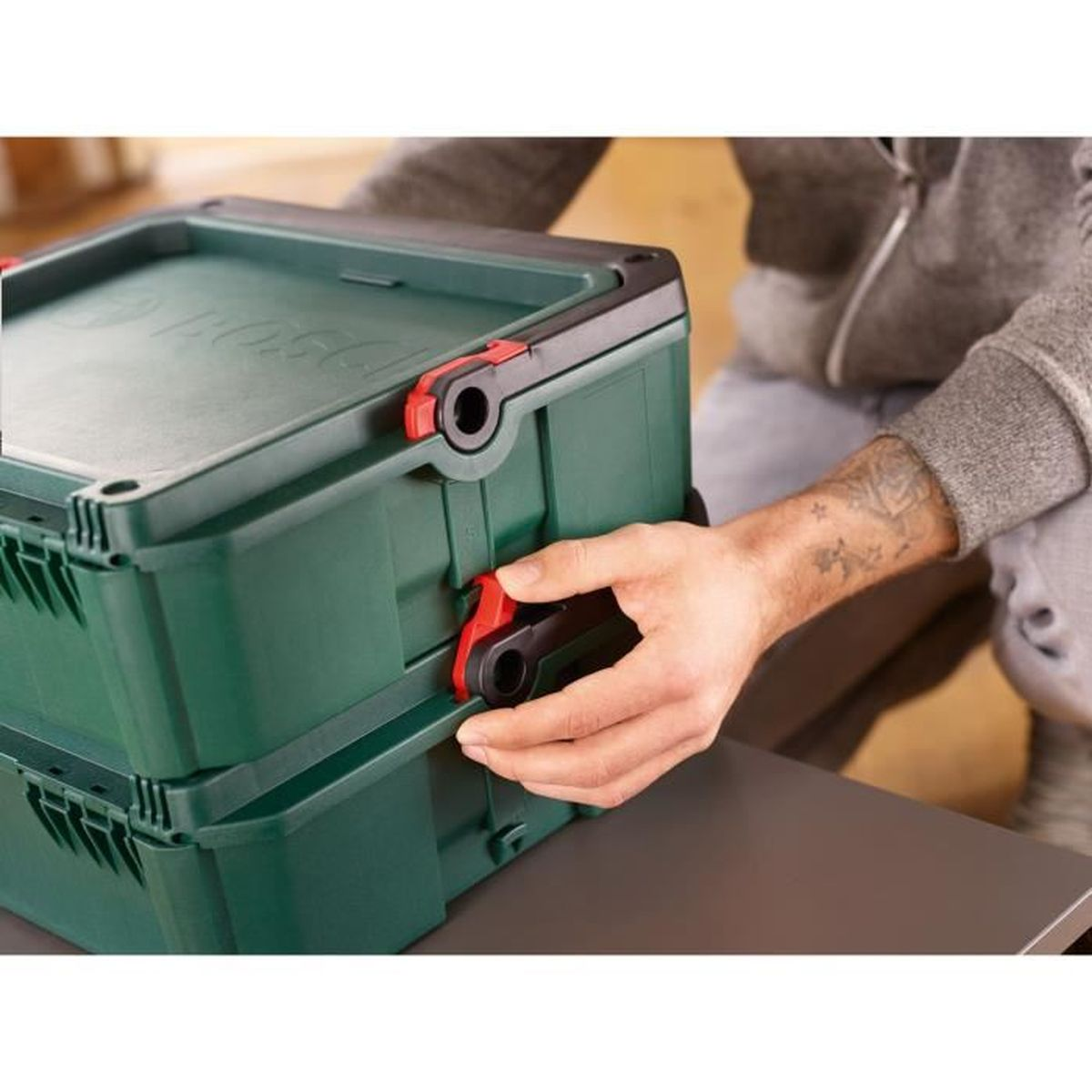 Un uomo aggancia una cassetta degli attrezzi Bosch verde. Primo piano.