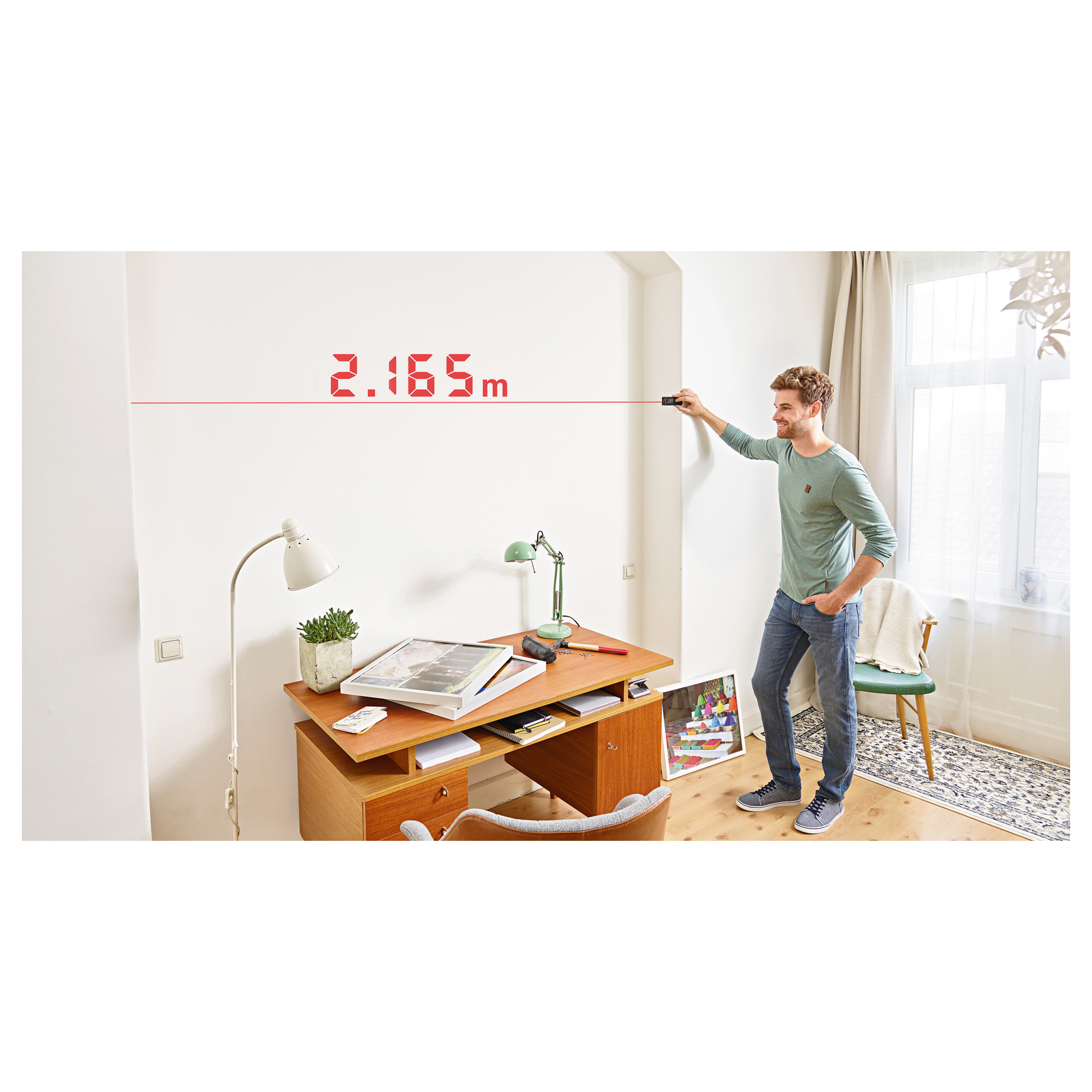 Mann misst Wand mit Laser: 2.165m. Schreibtisch daneben.