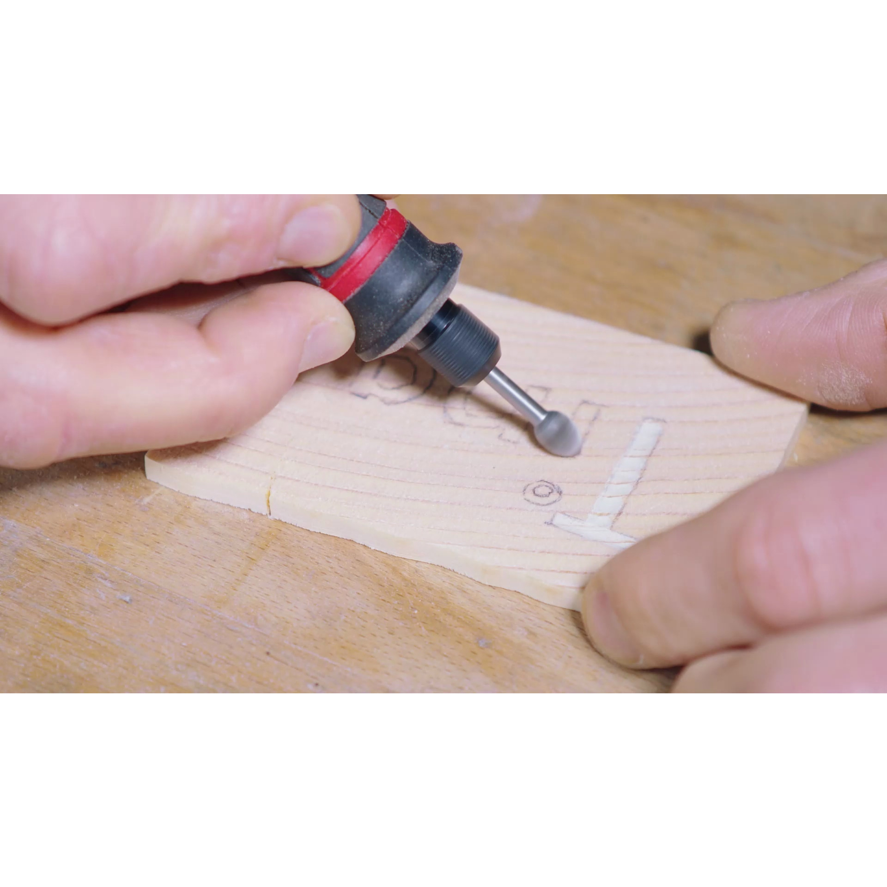 Mains utilisant un outil rotatif pour sculpter du bois avec des marques légères.