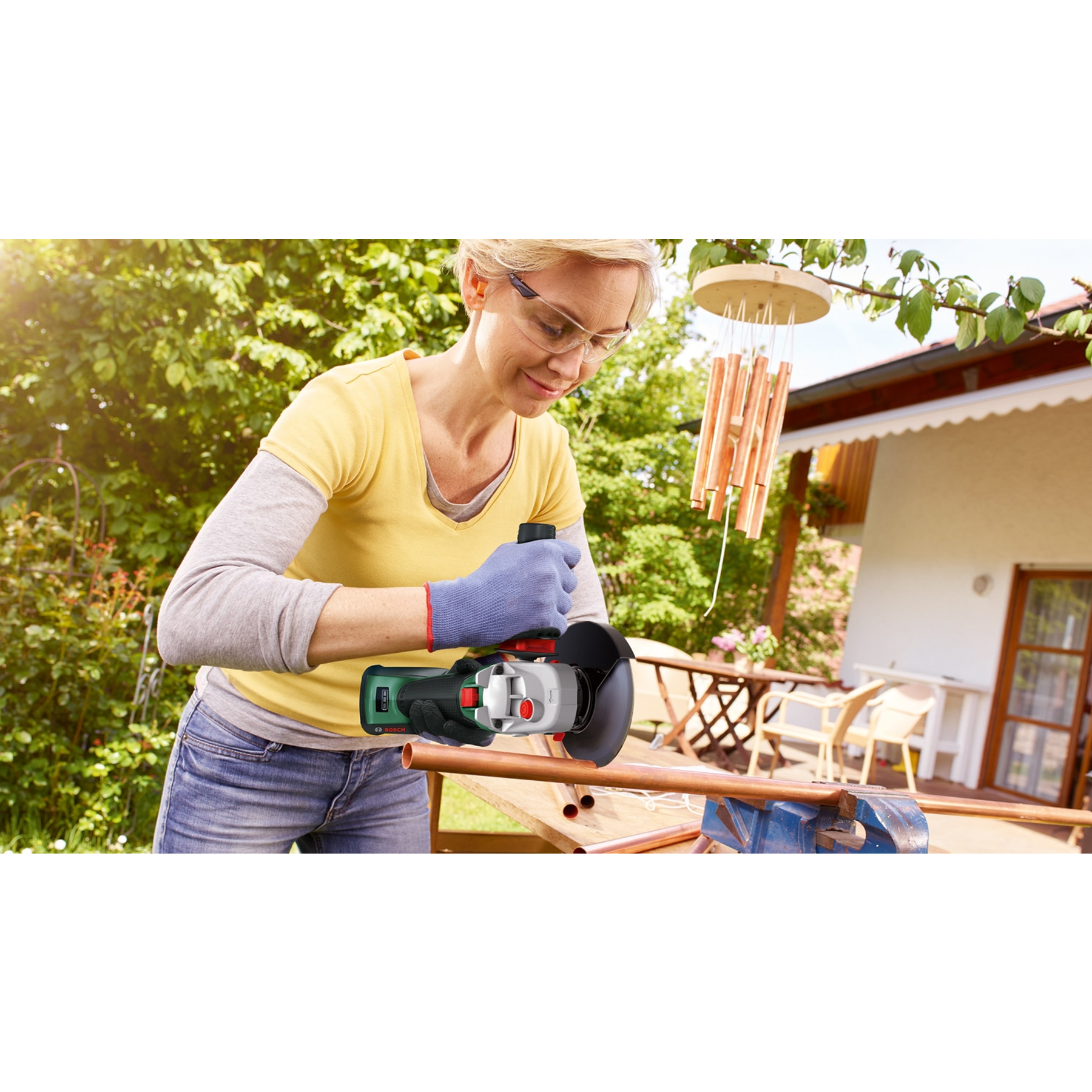 Frau schneidet Kupferrohr mit Winkelschleifer im Garten. Sommerliche Szene.