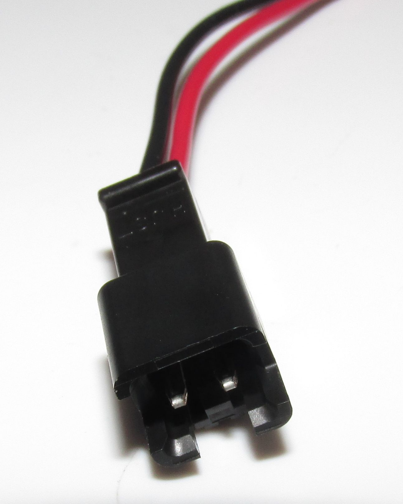Schwarzer Stecker mit roten und schwarzen Kabeln auf weißem Hintergrund.