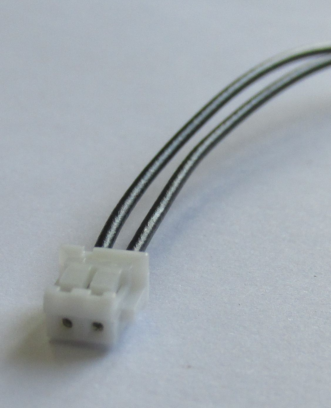Zwei schwarze Kabel führen aus einem kleinen weißen Stecker.