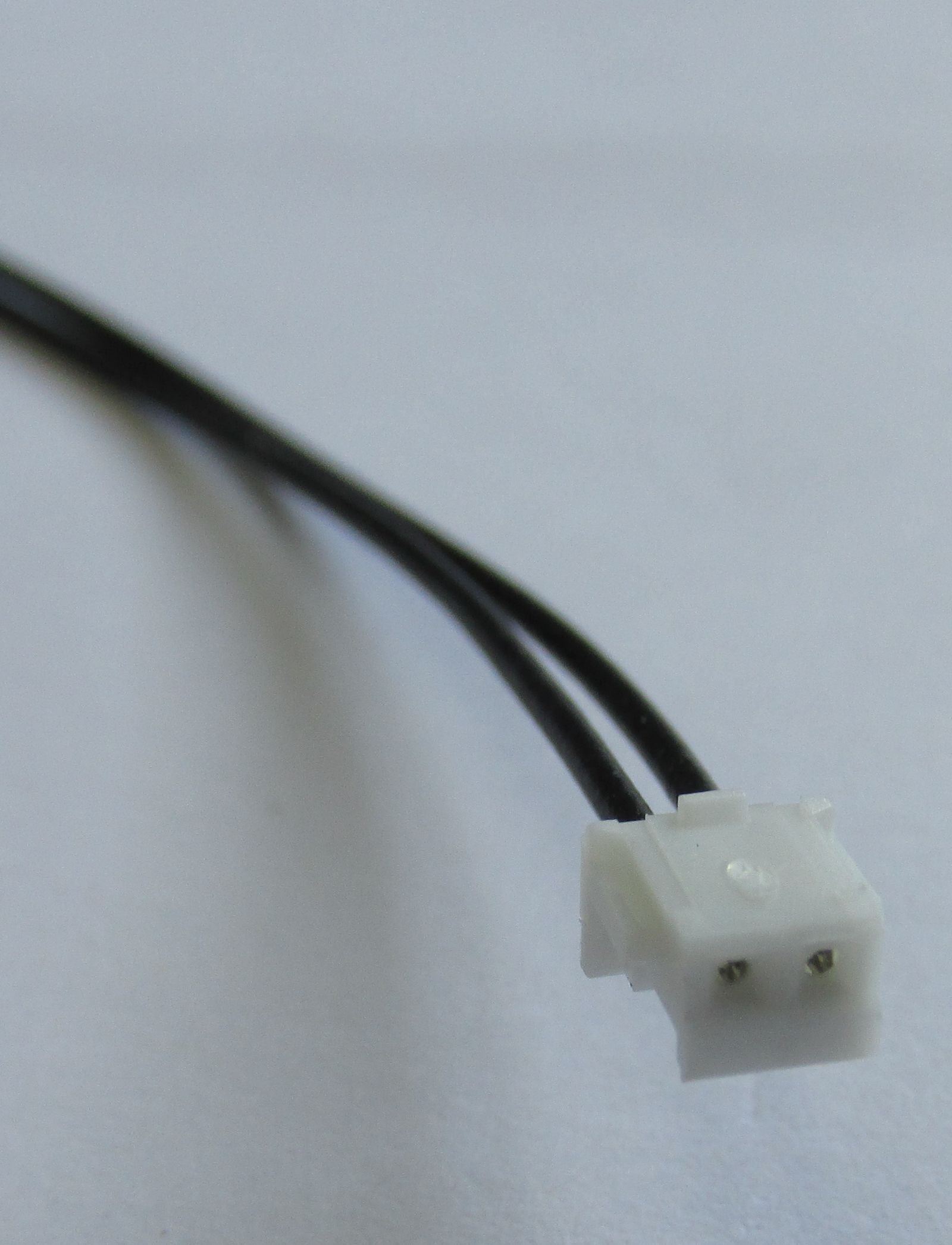 Ein weißer Stecker mit zwei schwarzen Kabeln auf grauem Hintergrund.