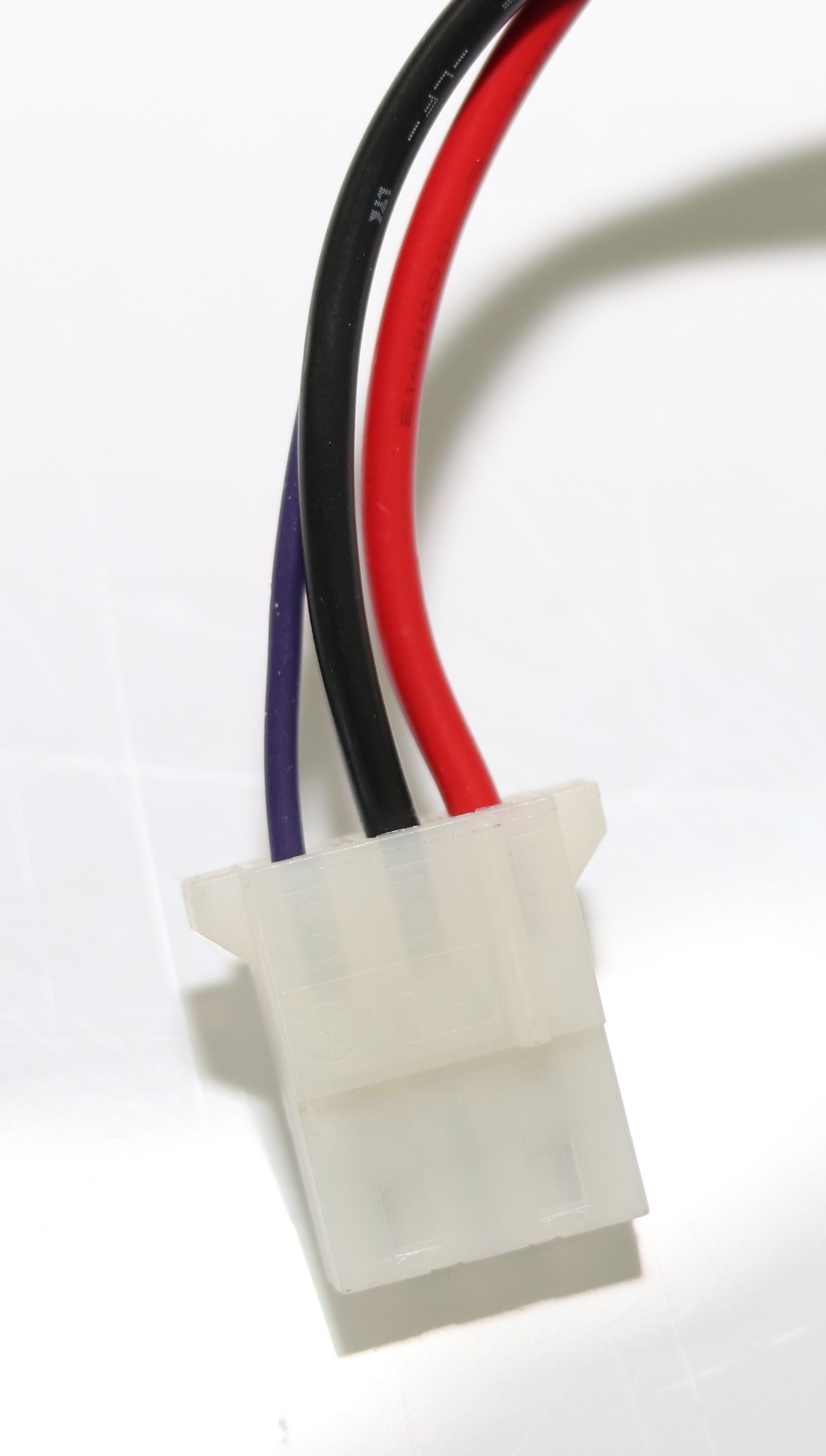 Ein weißer Stecker mit drei farbigen Kabeln: rot, schwarz und violett.