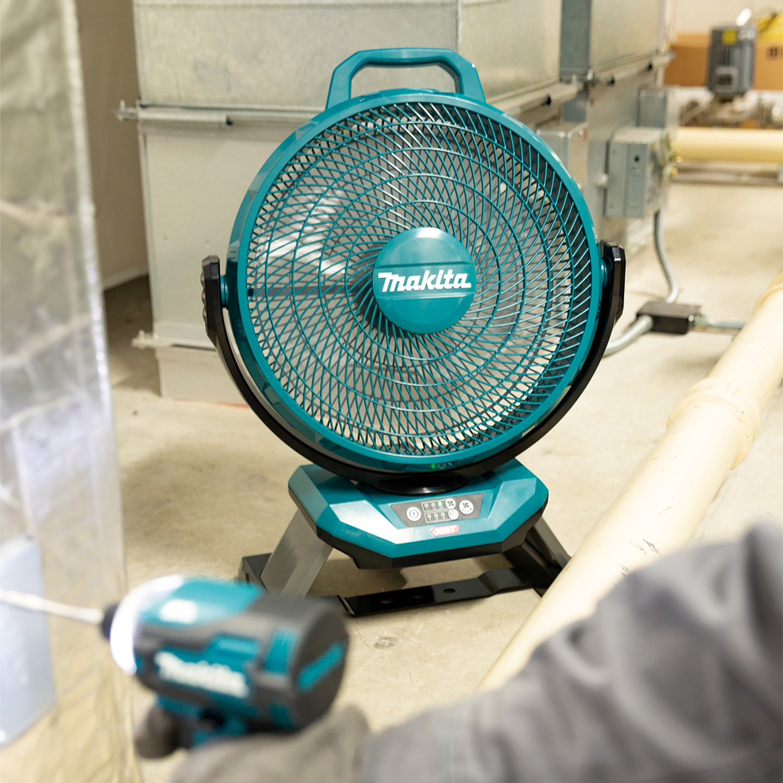 Una ventola Makita color turchese su pavimento in cemento vicino a un attrezzo.