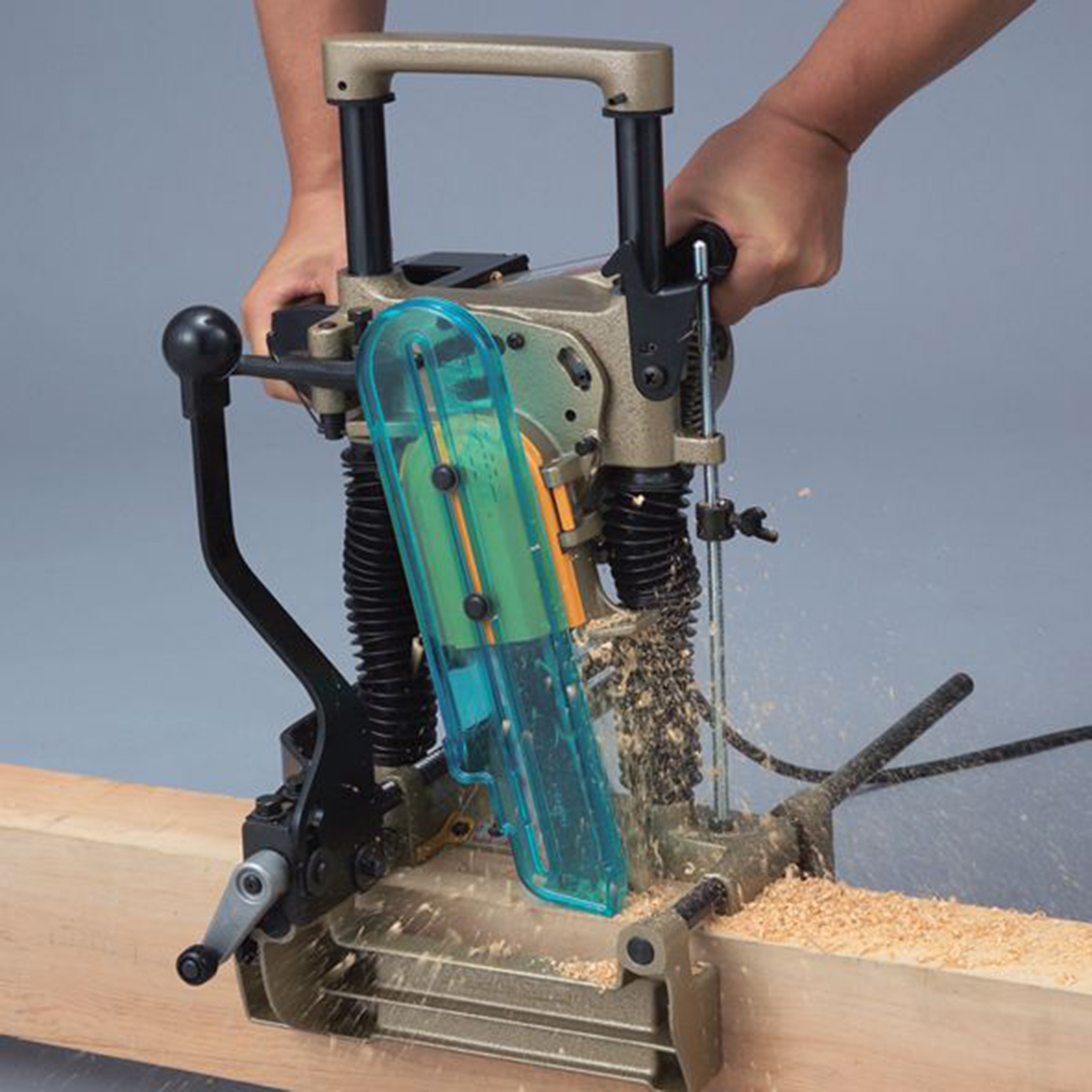 Holzbearbeitungsmaschine bohrt Holz, Späne fliegen, Hände bedienen Hebel.