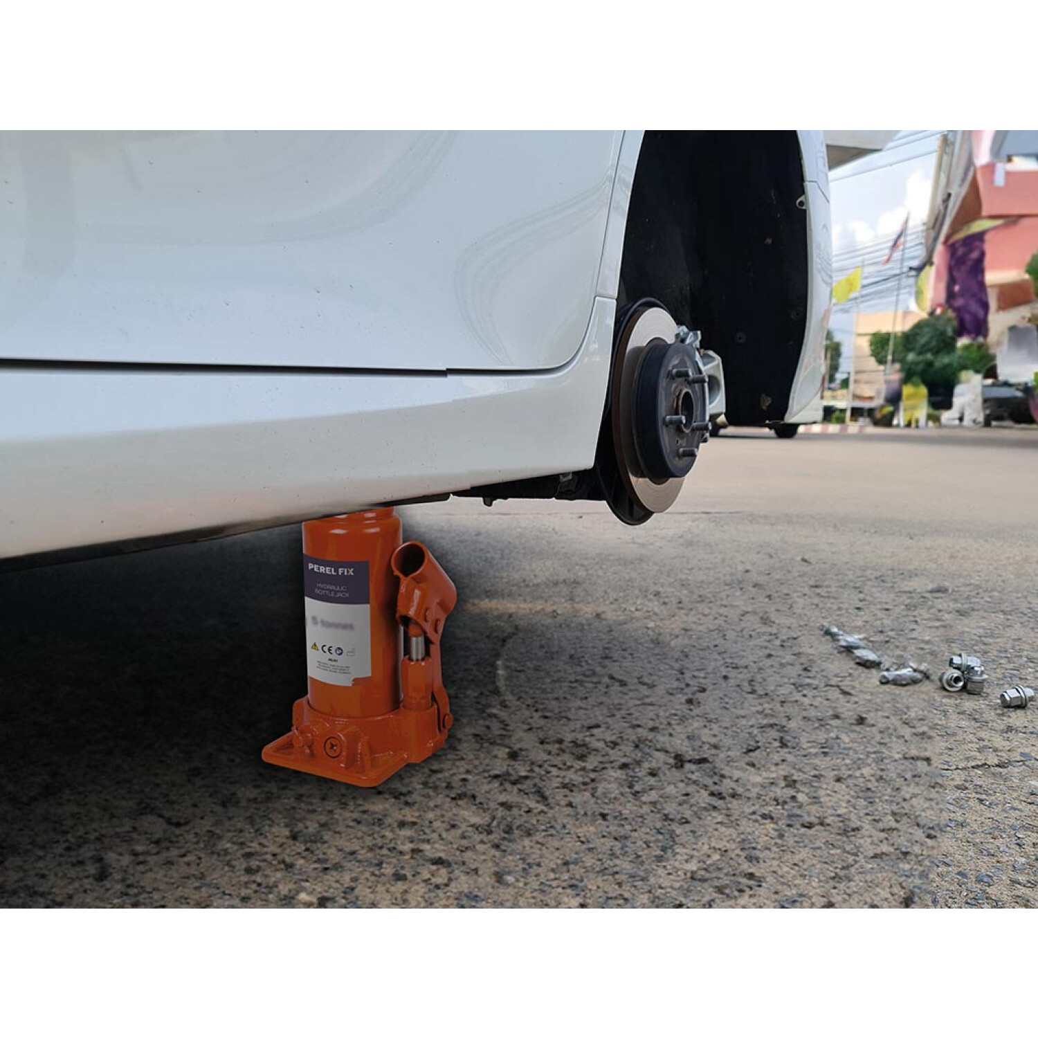 Un cric arancione solleva un'auto bianca con la ruota rimossa.