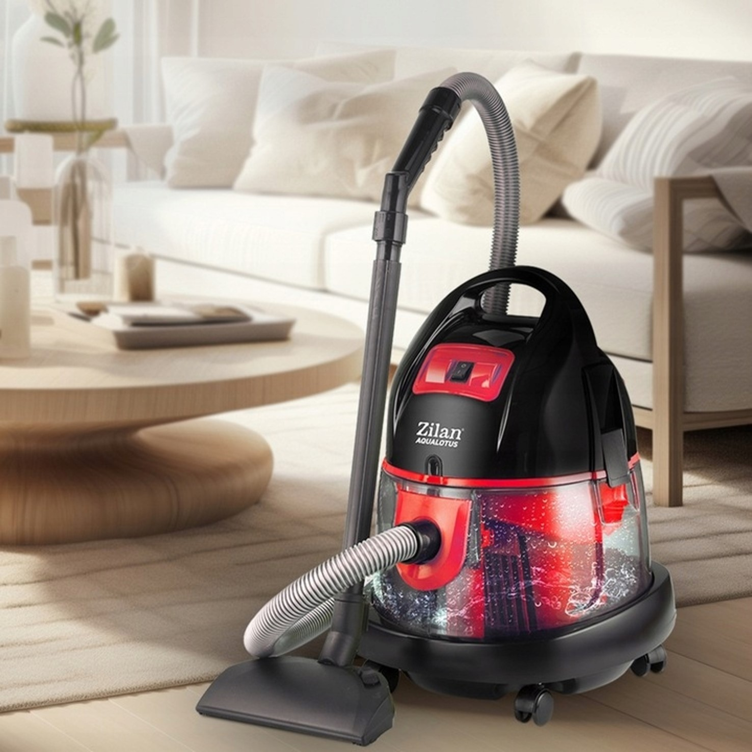 Czarno-czerwony odkurzacz z wężem stoi na dywanie obok sofy.